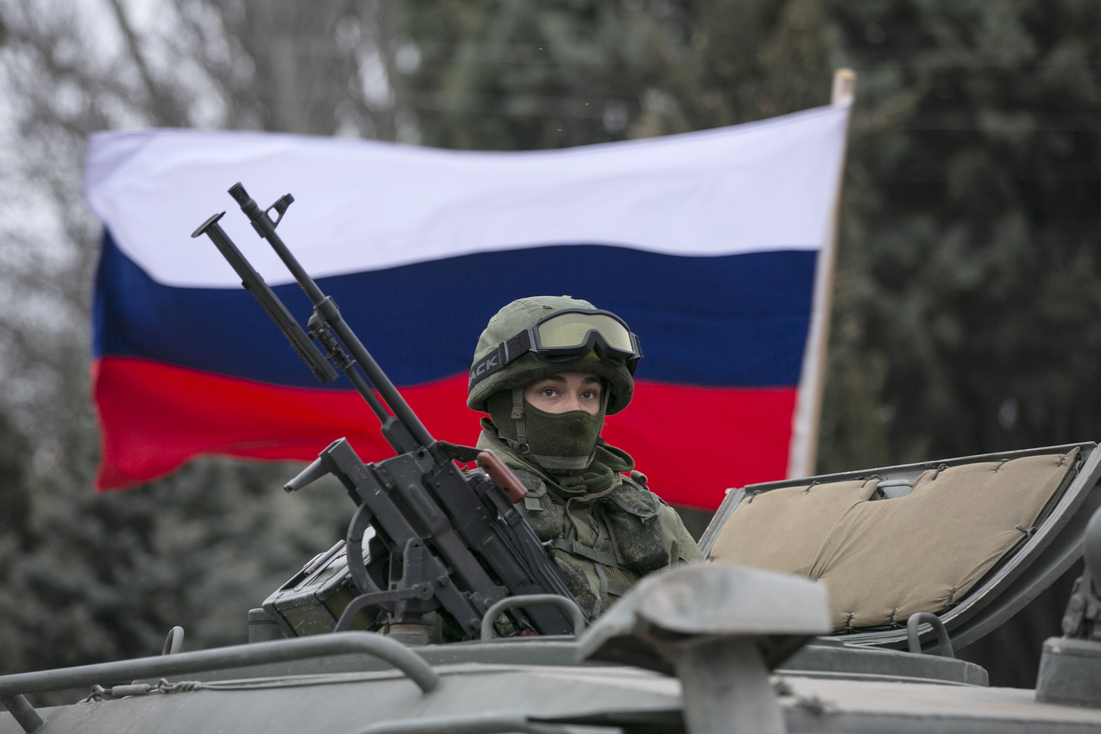 A pro-Russian man (not seen) holds a Russian flag behind an armed serviceman on top of a Russian army vehicle outside a Ukrainian border guard post in the Crimean town of Balaclava