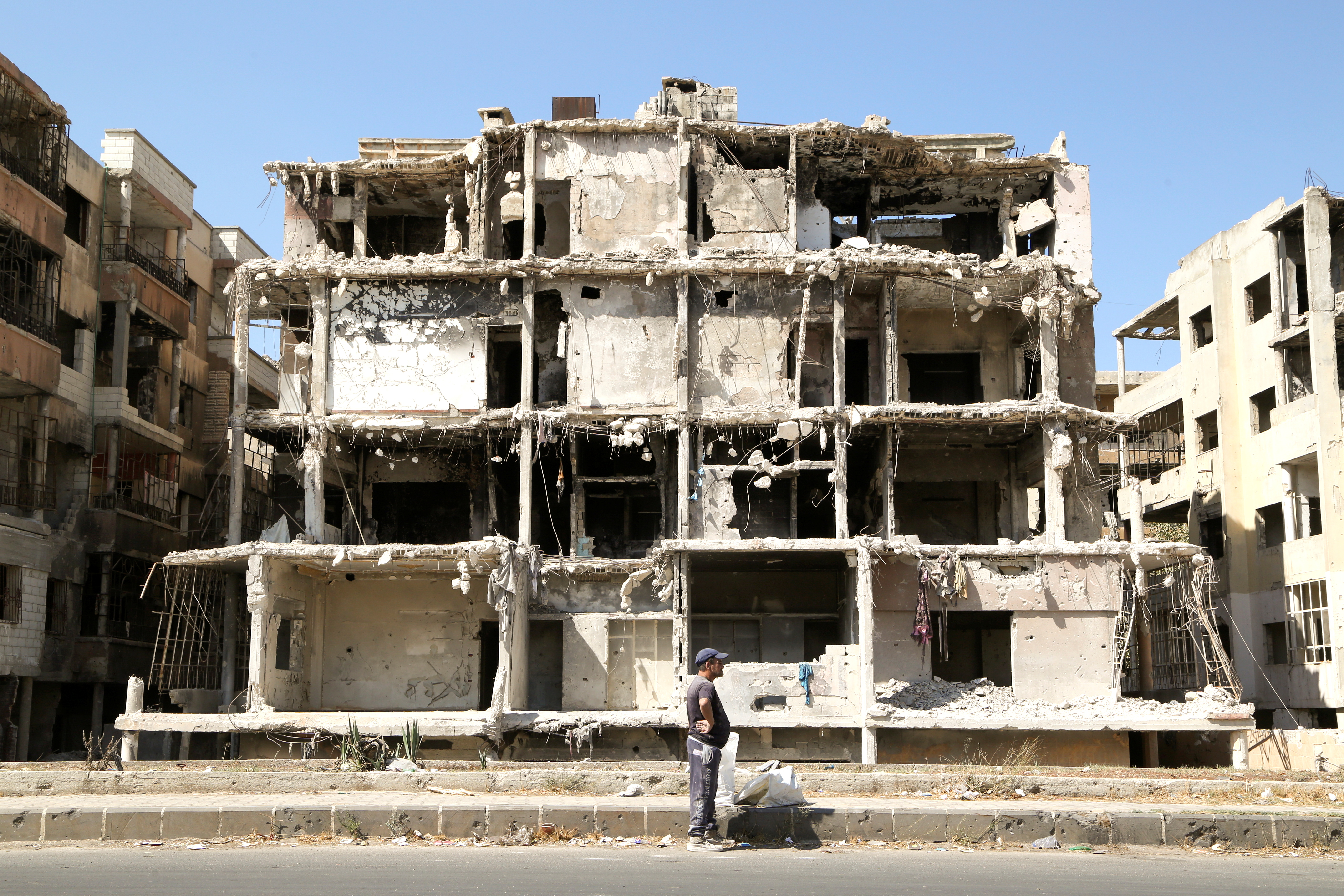 A man stands past a damaged building in Homs, Syria, October 3, 2021
