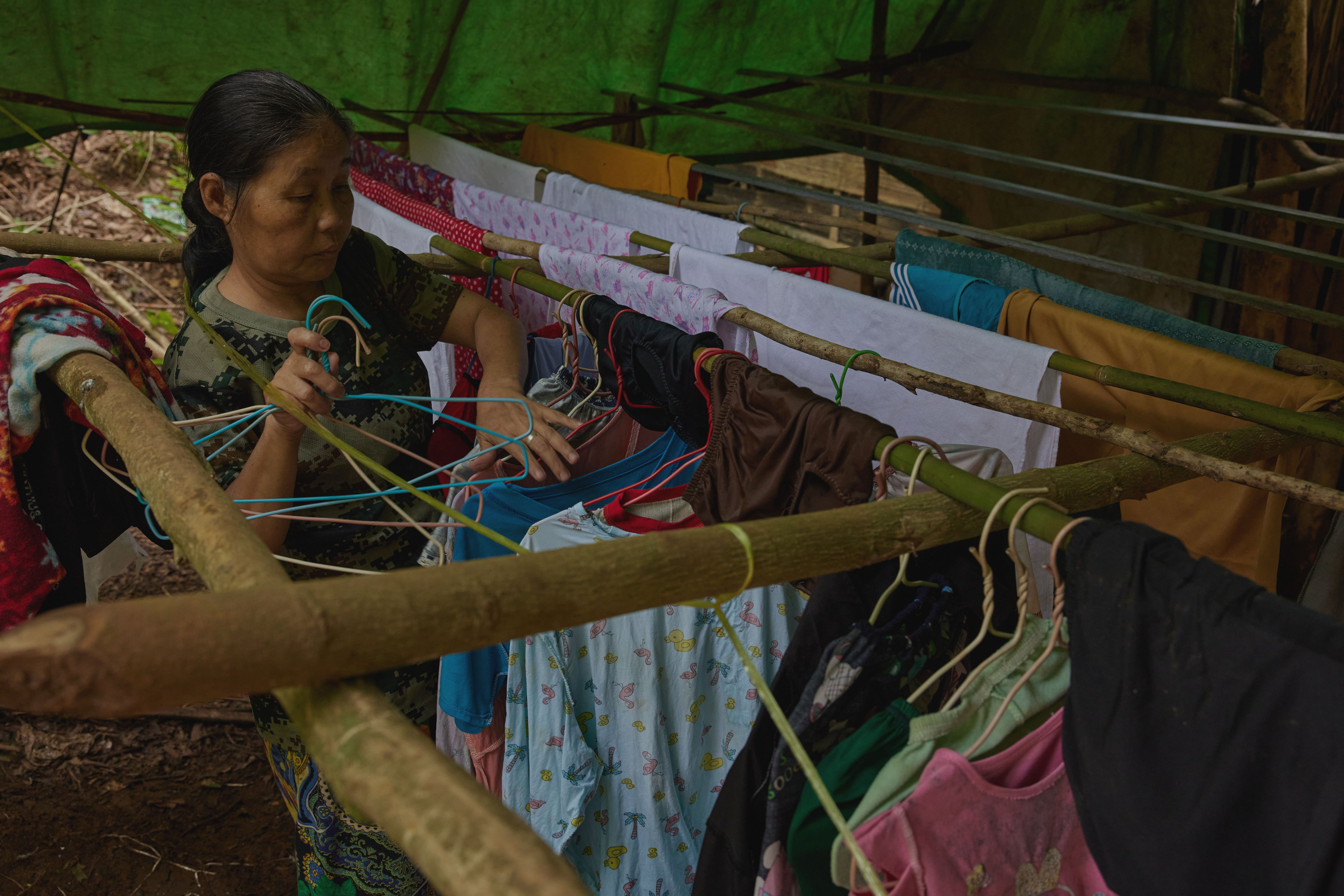 A woman hangs out her washing at her newly-constructed home in the jungle outside her village that she fled, Dae Pu Noh [Al Jazeera]