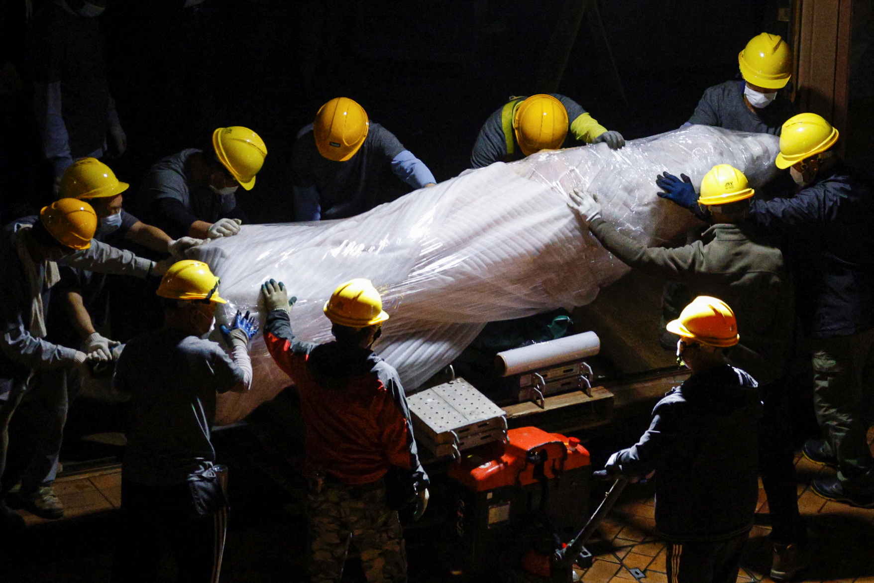 Nine workers in yellow contruction helmets remove the Pillar of Shame monument
