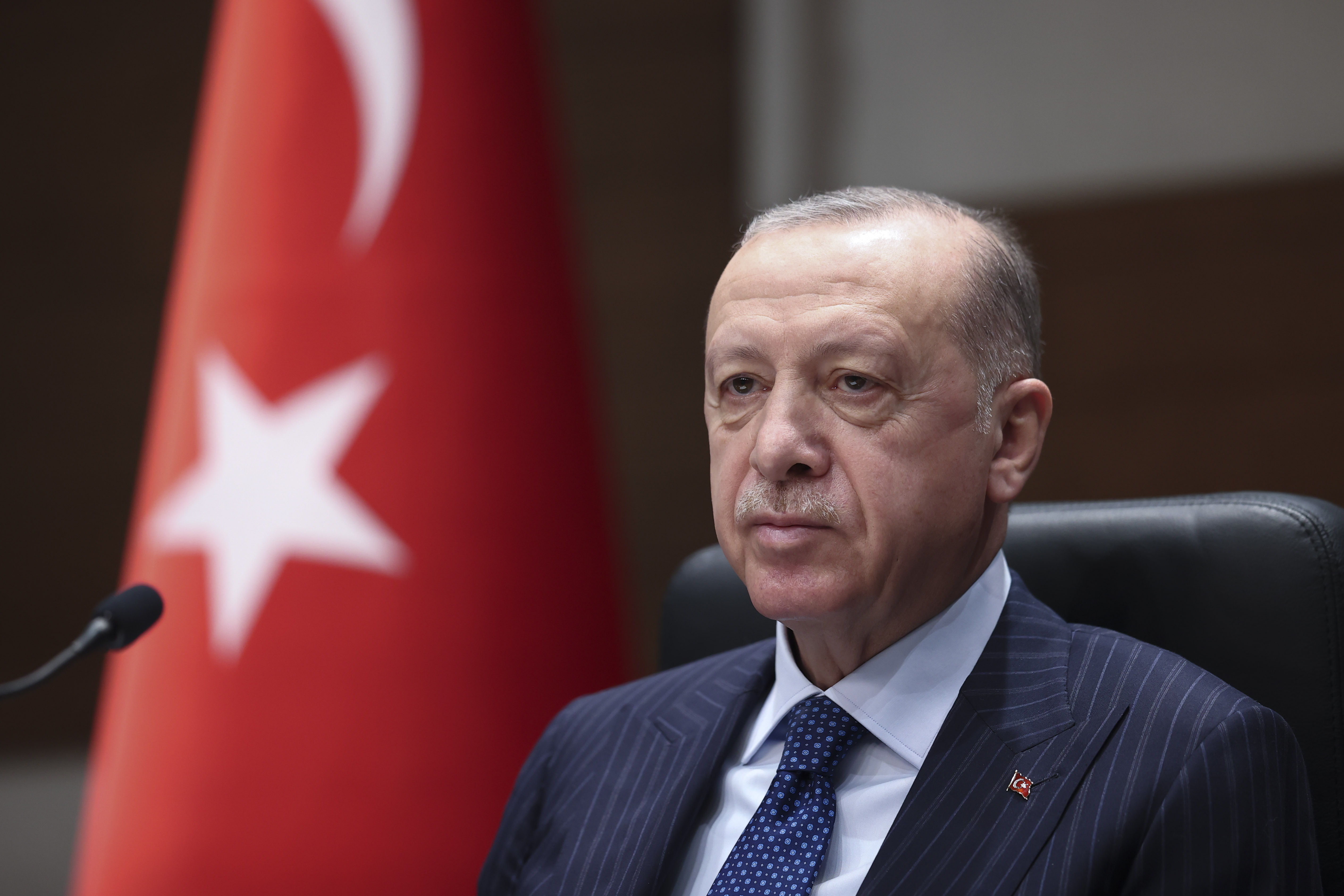 Turkish President Recep Tayyip Erdogan is seen sitting on a chair with a Turkish flag in the background