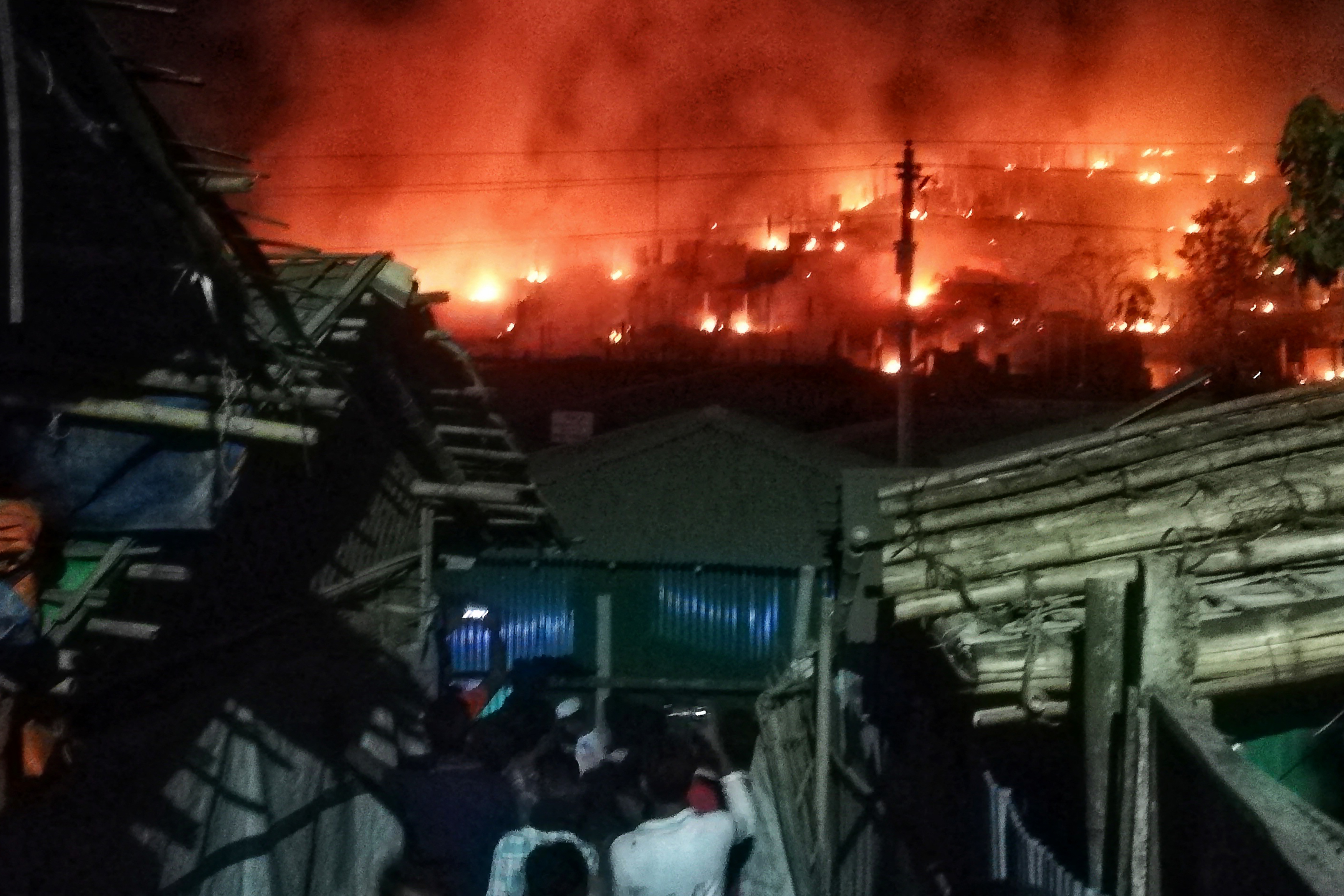 Onlookers gather as smoke and flames can be seen on a hillside after a fire broke out in a Rohingya refugee camp in Ukhia on January 9, 2022 [AFP]