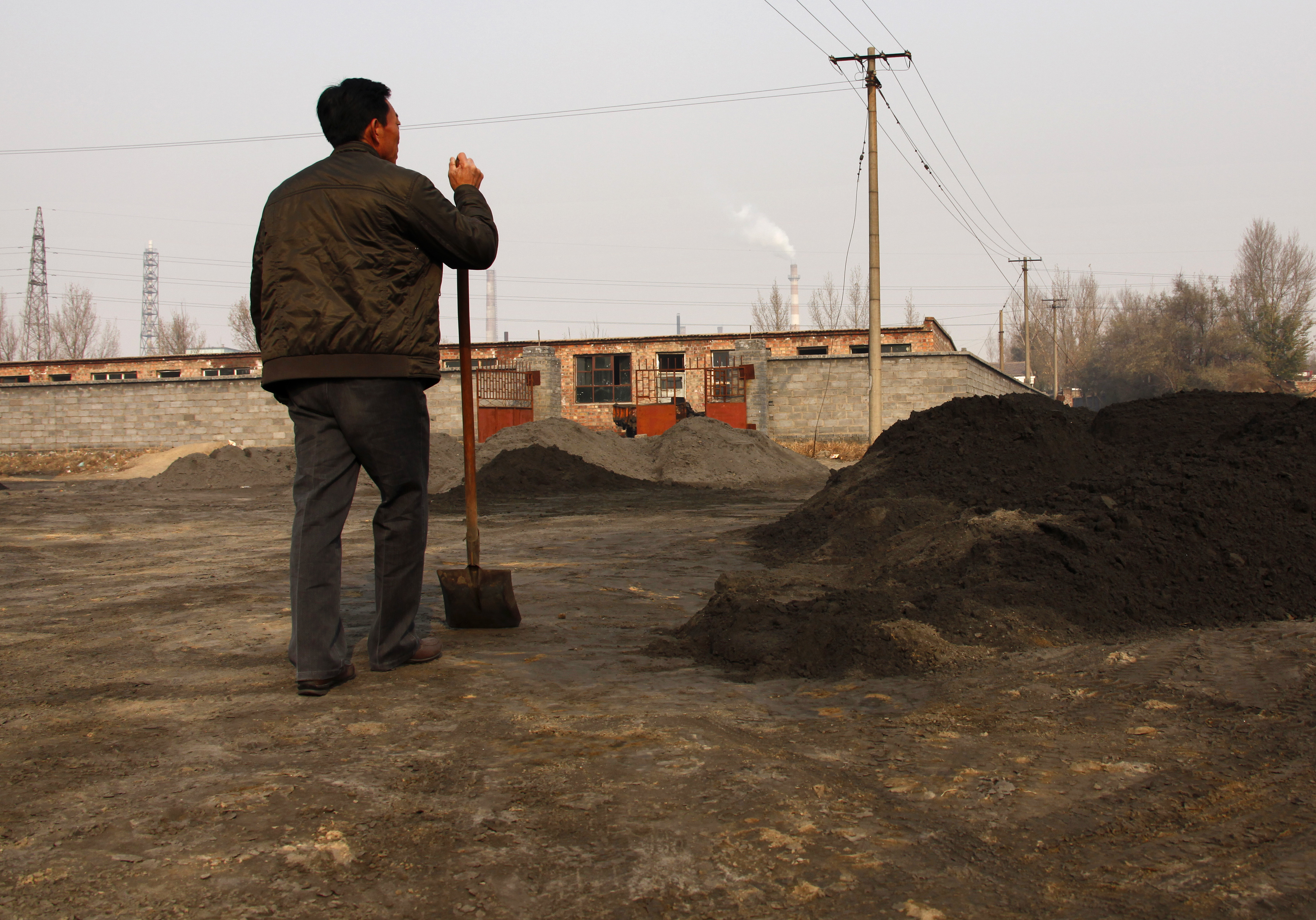 A villager looks towards a rare earth smelting plant as he takes a break from shovelling in China
