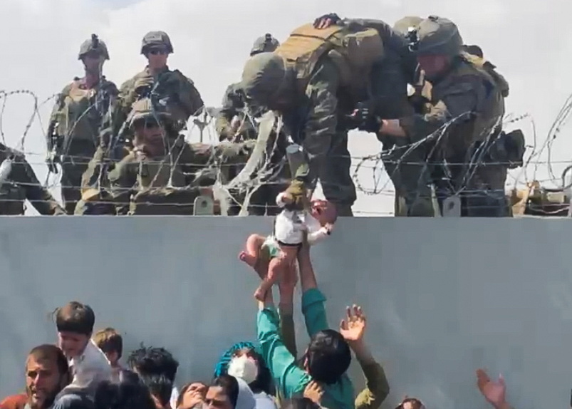 A baby is handed over to the American army over the wall of Kabul airport.