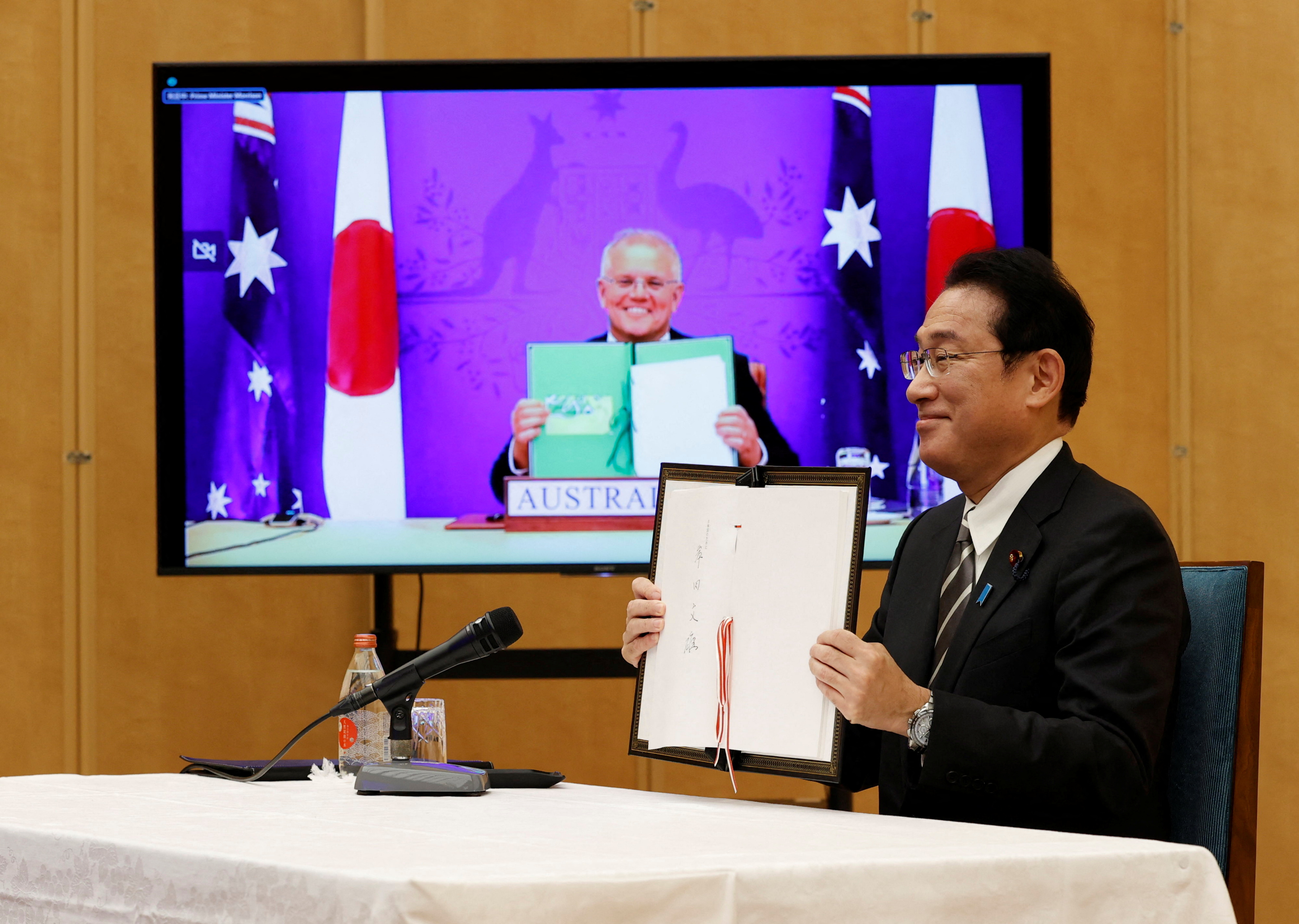 Japan's Prime Minister Fumio Kishida and Australia's Prime Minister Scott Morrison show off signed documents during their video signing ceremony of the bilateral reciprocal access agreement