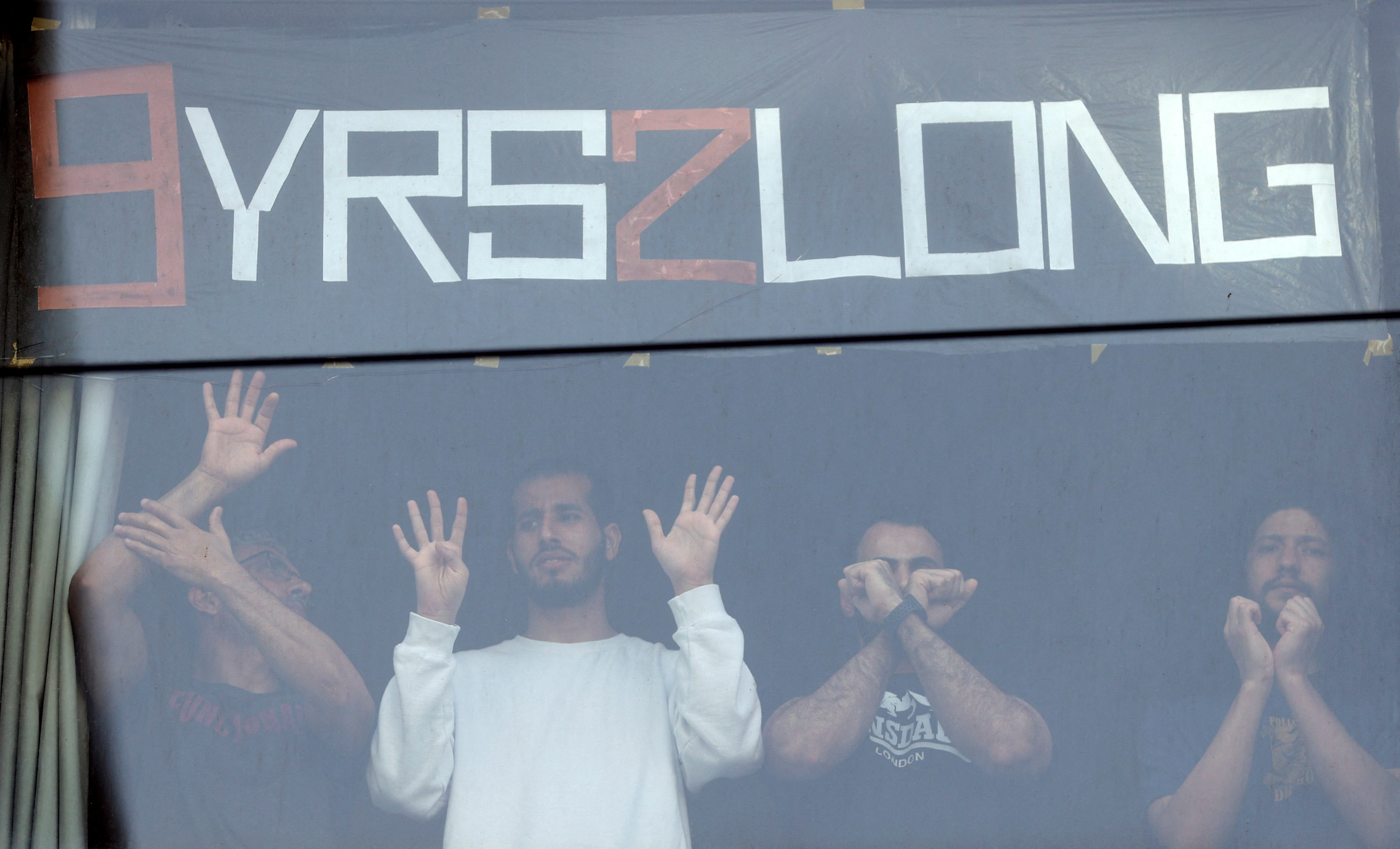 People standing in a window gesture toward pro-refugee protestors demonstrating outside the Park Hotel, where Serbian tennis player Novak Djokovic is believed to be held while he stays in Australia, in Melbourne