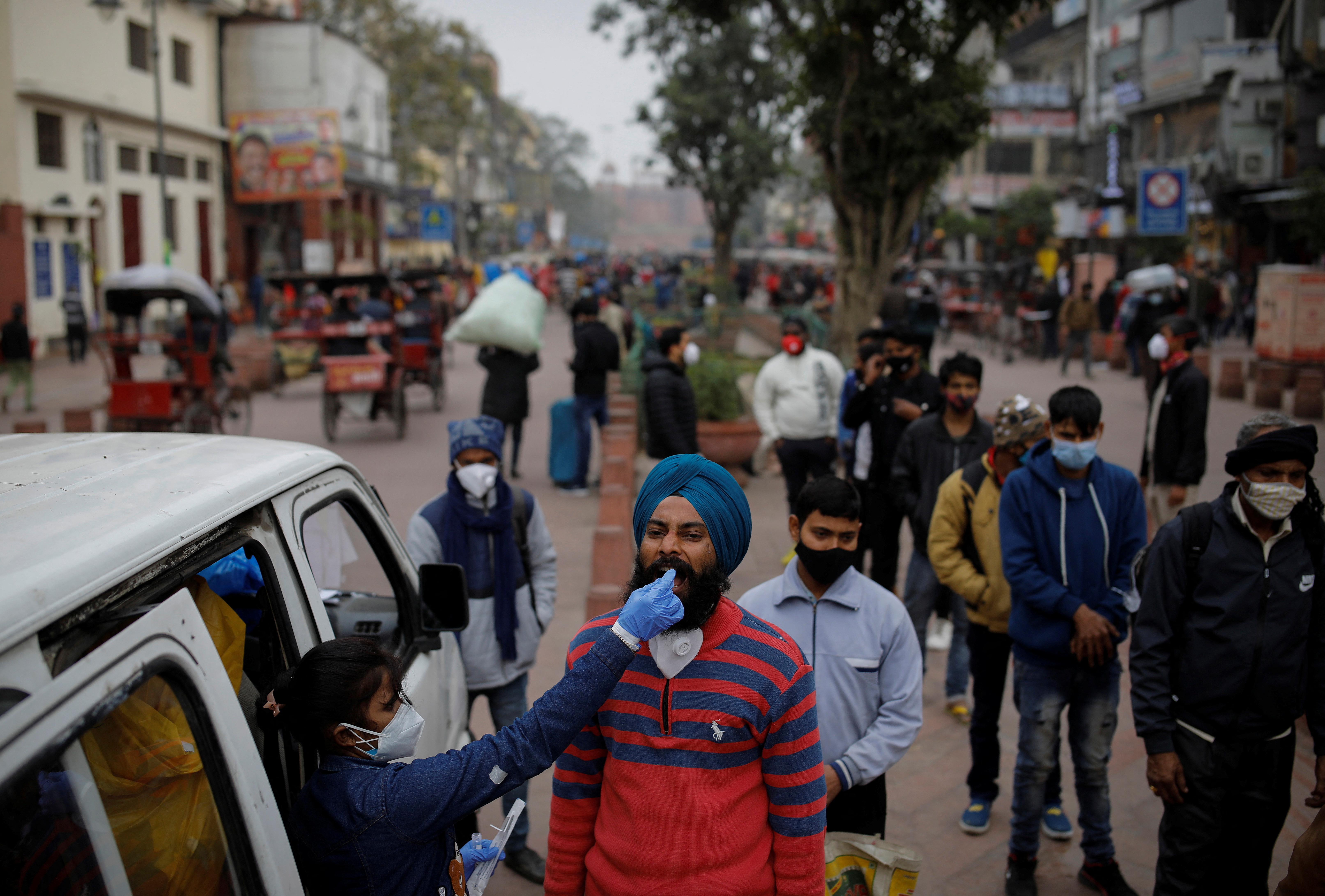 A healthcare worker collects a swab sample from a man as others wait at a market area in the old quarters of Delhi
