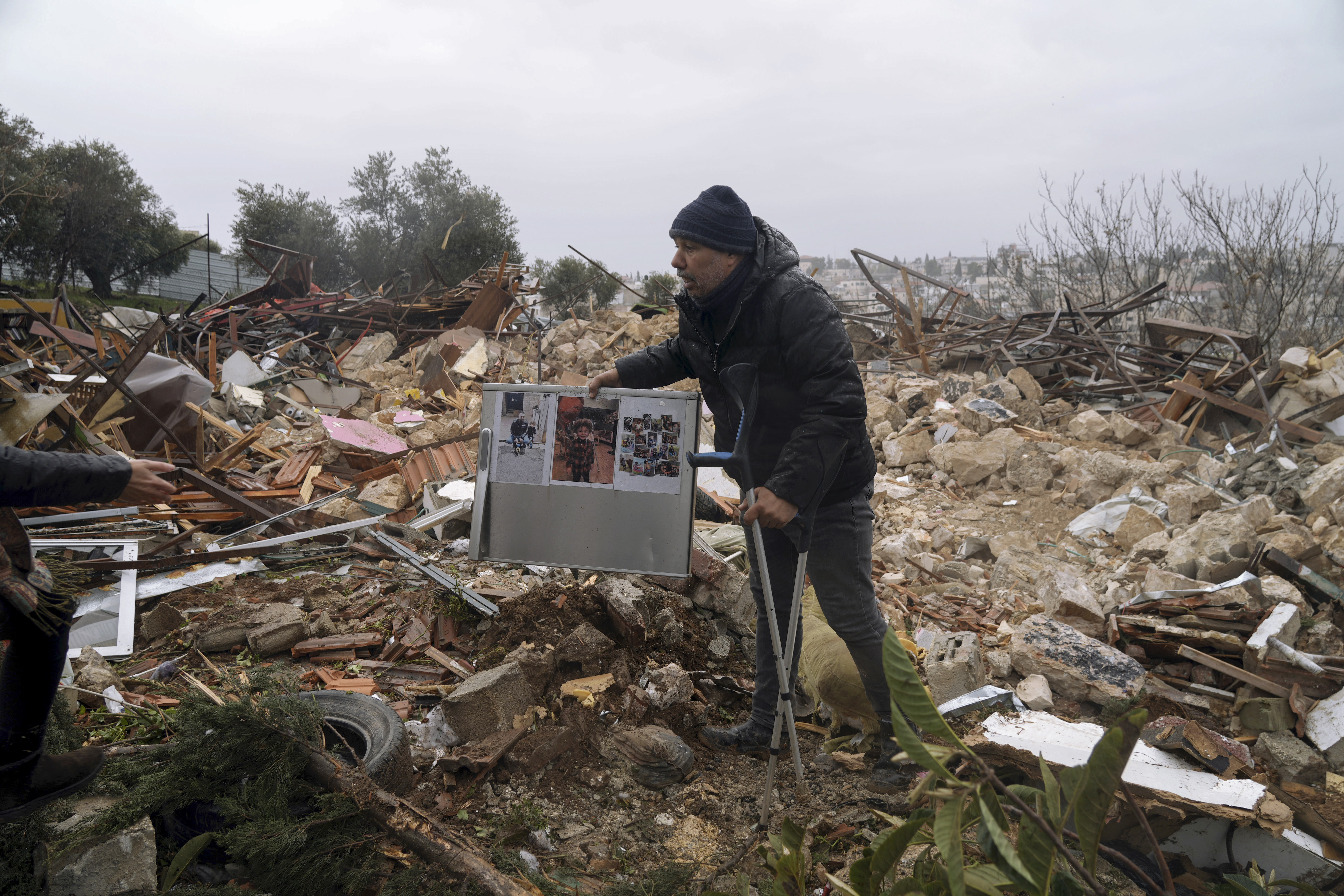 Local activist Mohammad Abu al-Hommos holds up family photos at the ruins of the Palestinian house demolished by Israeli forces in the flashpoint occupied east Jerusalem neighborhood of Sheikh Jarrah, Wednesday, Jan. 19, 2022.