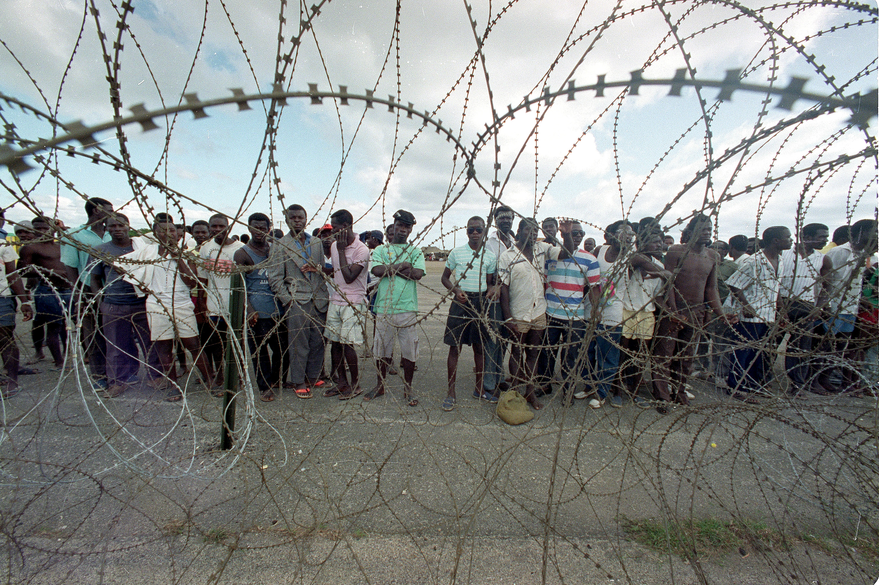 Scores of Haitian refugees stand behind razor wire at the Guantanamo Bay Naval Base in Cuba on December 29, 1991. The men were rescued in international waters by the United States Coast Guard after fleeing economic hardship in Haiti