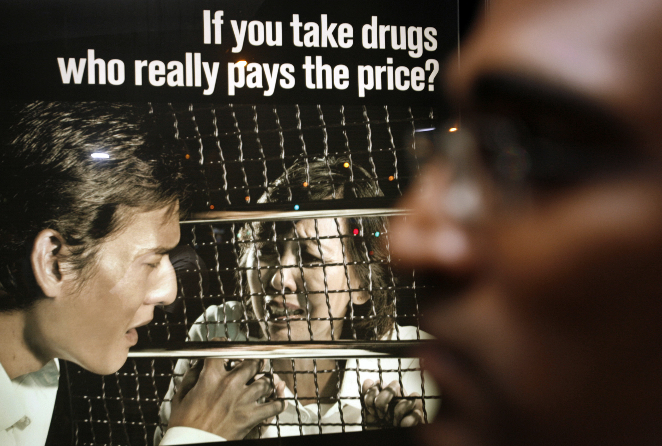 Profile of M Ravi walking past a drug prevention advertisement during a vigil for Nigerian Iwuchukwu Amara Tochi in 2007