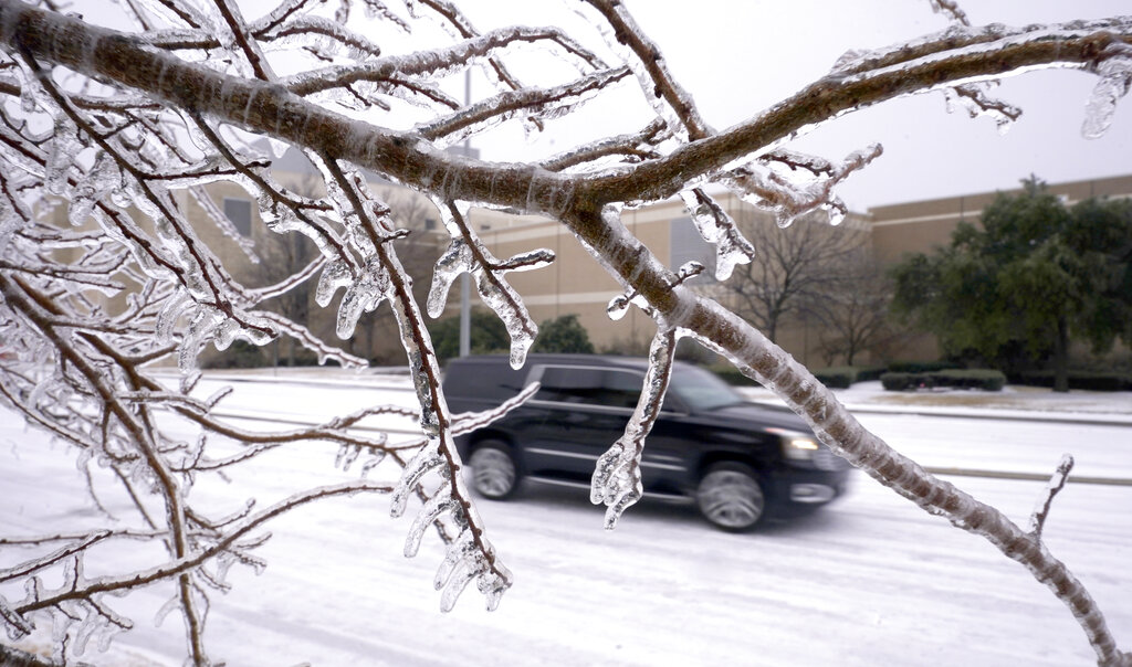 Ice coats trees and the road as an SUV drives on a snow-covered road in Richardson, Texas