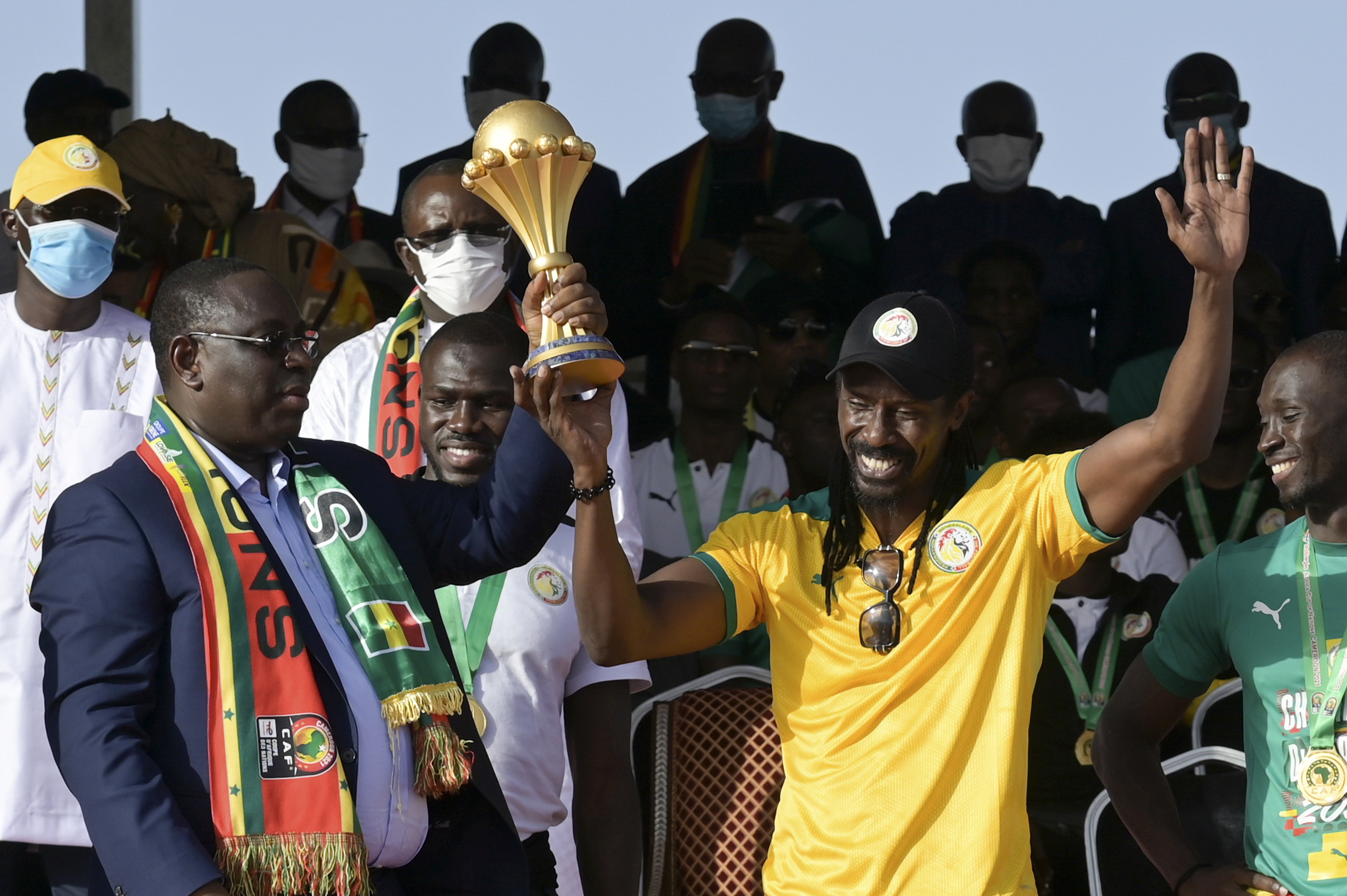 Senegal’s President Macky Sall, left, and coach Aliou Cisse, right), hold the AFCON trophy during a ceremony after the national football team arrived back at the airport in Dakar
