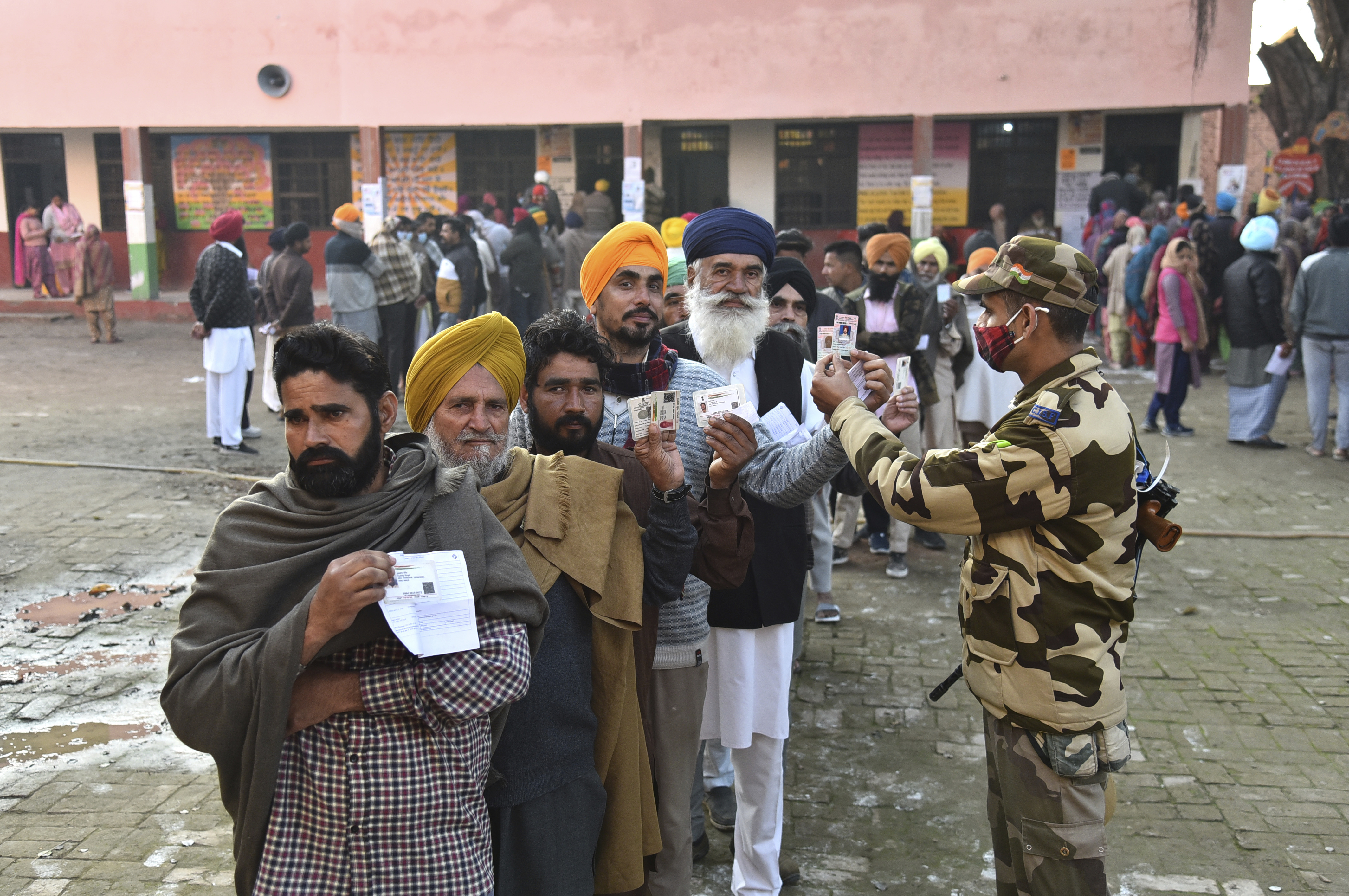 A paramilitary soldier checks identity cards of voters standing in a queue outside a polling station at Attari village, about 45km (25 miles) from Amritsar, Punjab