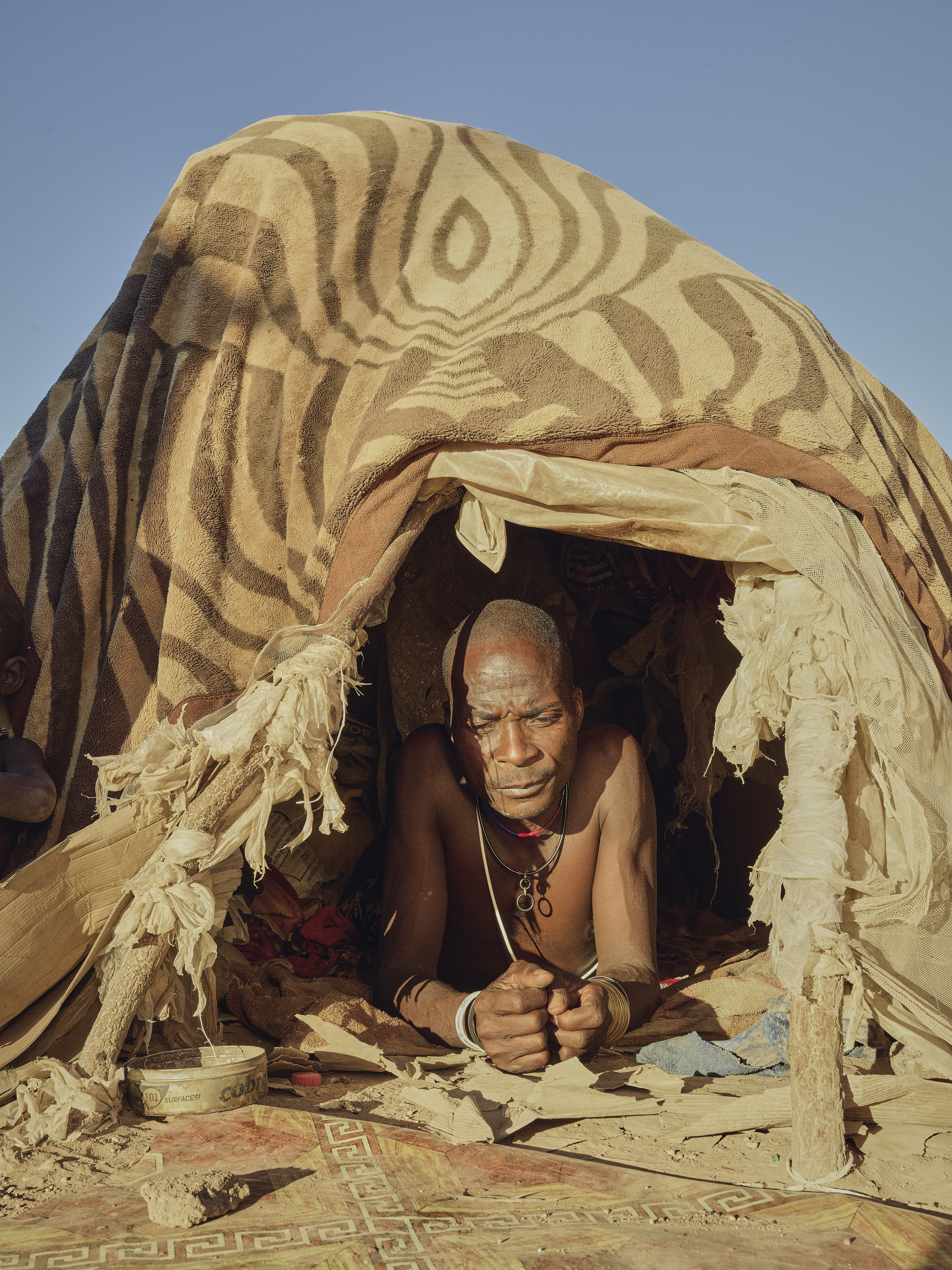 A photo of a refugee man peeking through the tent that he is in.