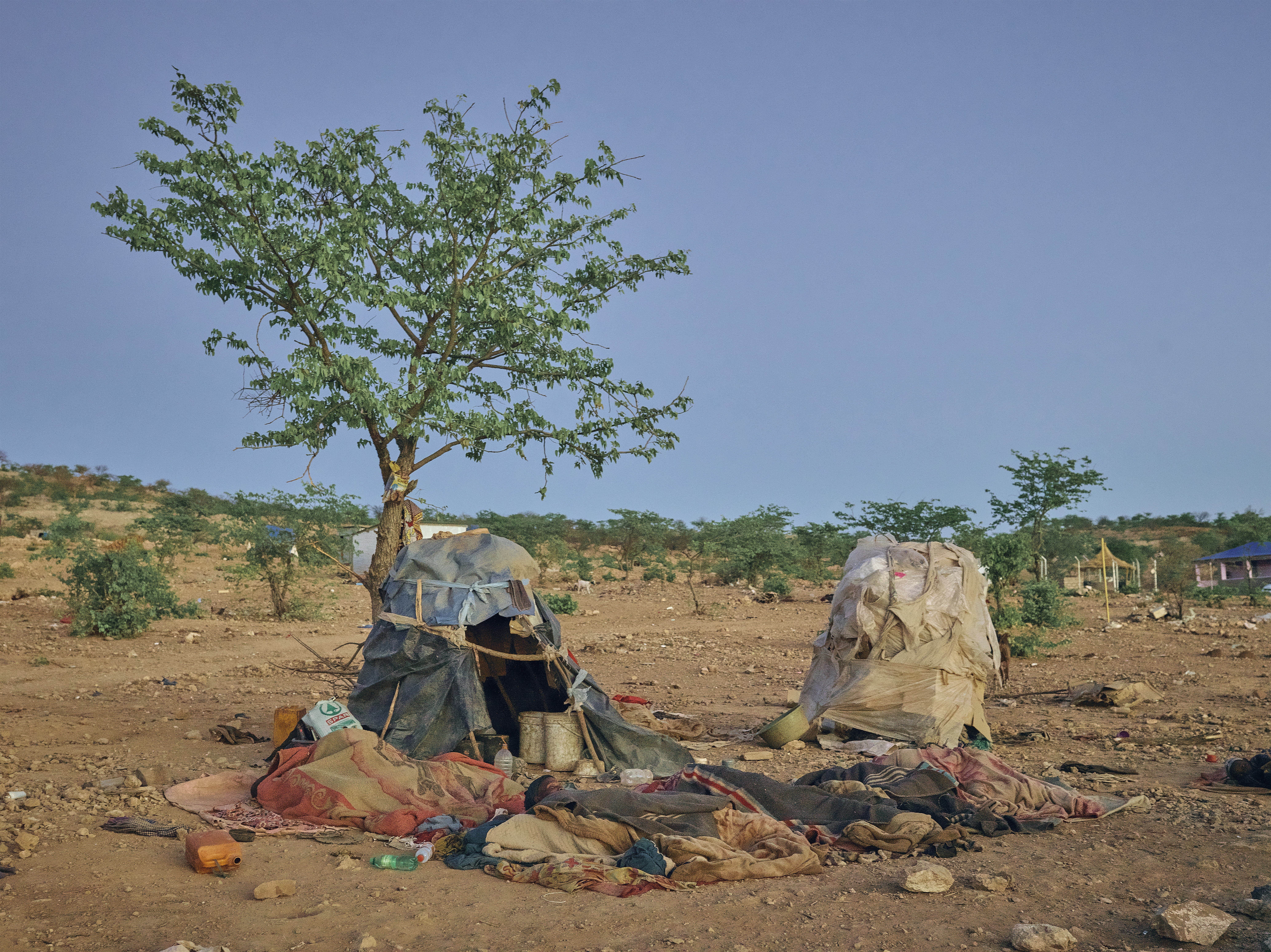 A photo of two tents and people sleeping on a blanket next to them.