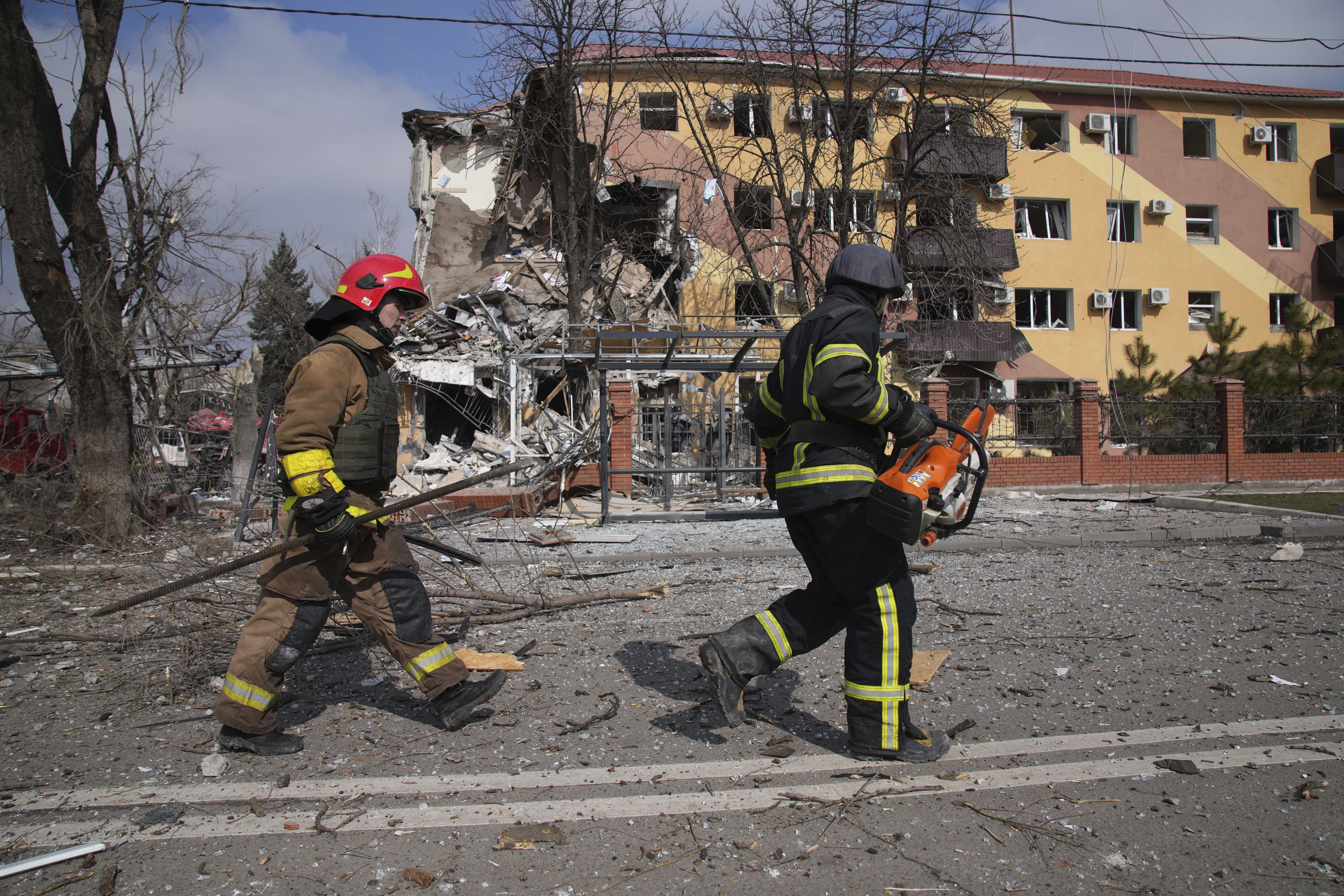 Firefighters walk past a building damaged by shelling in Mariupol, Ukraine, on Thursday