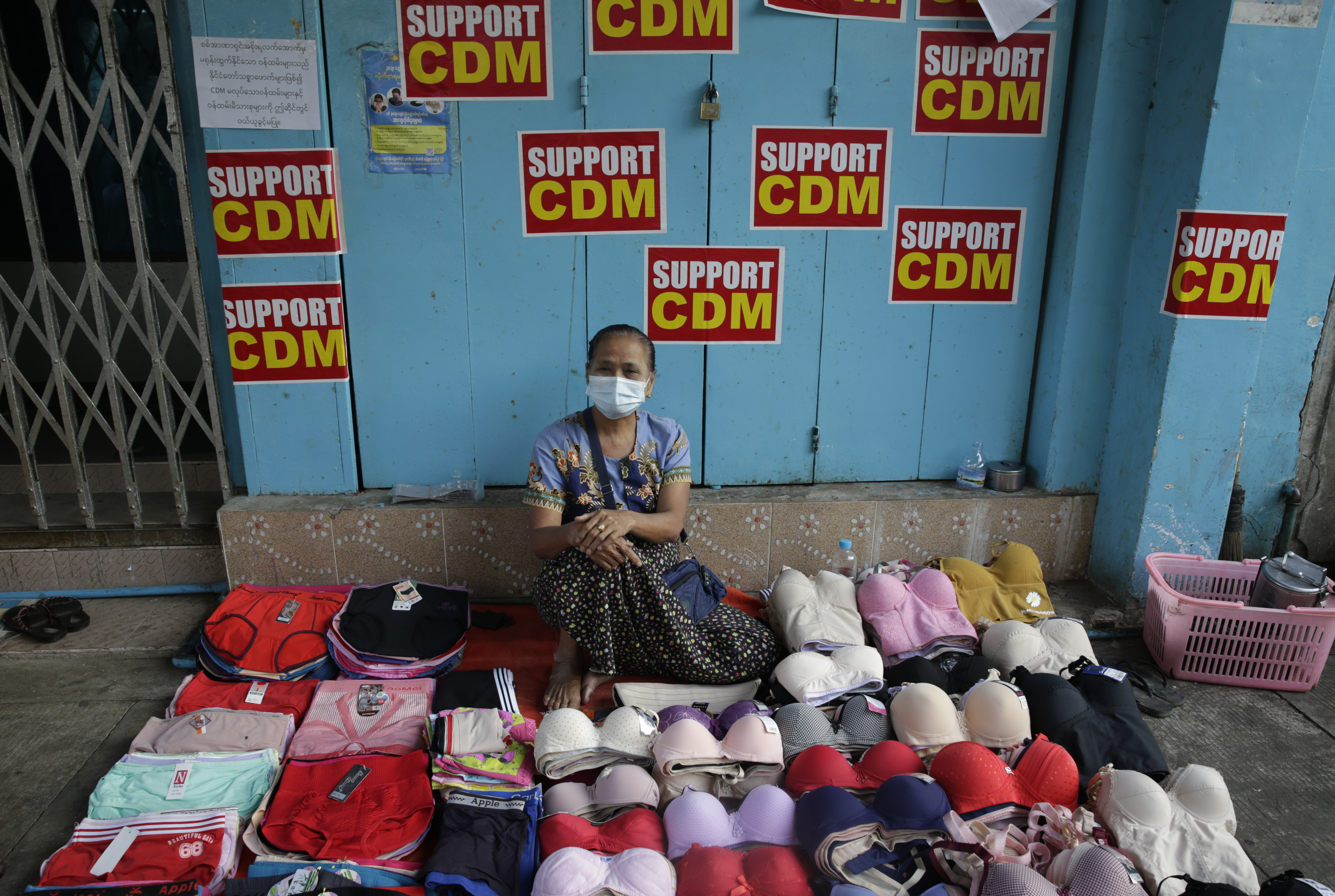 A woman sits behind her stall selling underwear on the street in Yangon in front of posters calling for mass civil disobedience