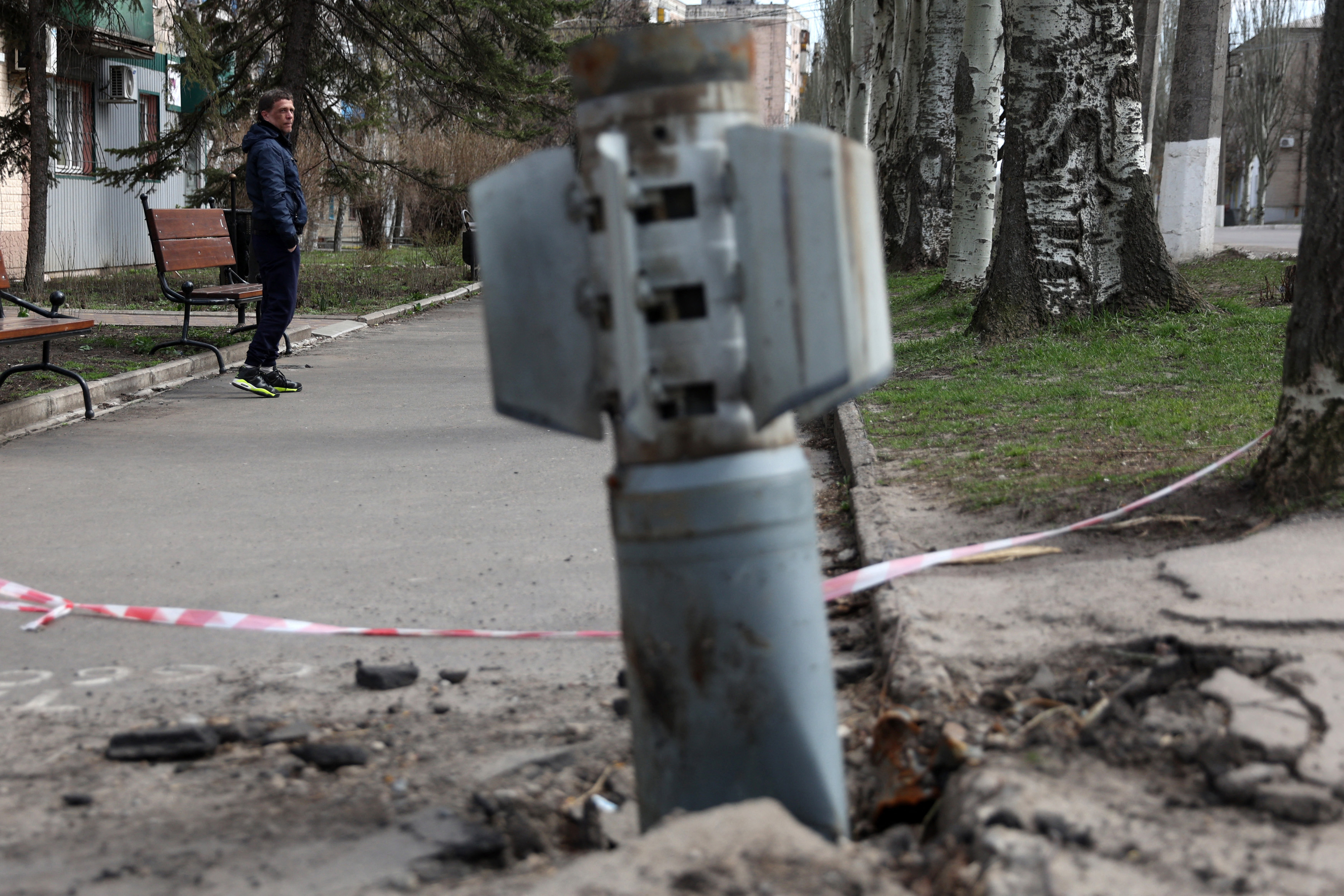 A man walks past an unexploded tail section of a 300mm rocket that appears to have contained cluster bombs launched from a BM-30 Smerch multiple rocket launcher embedded in the ground after shelling in Lysychansk, Luhansk region on April 11, 2022