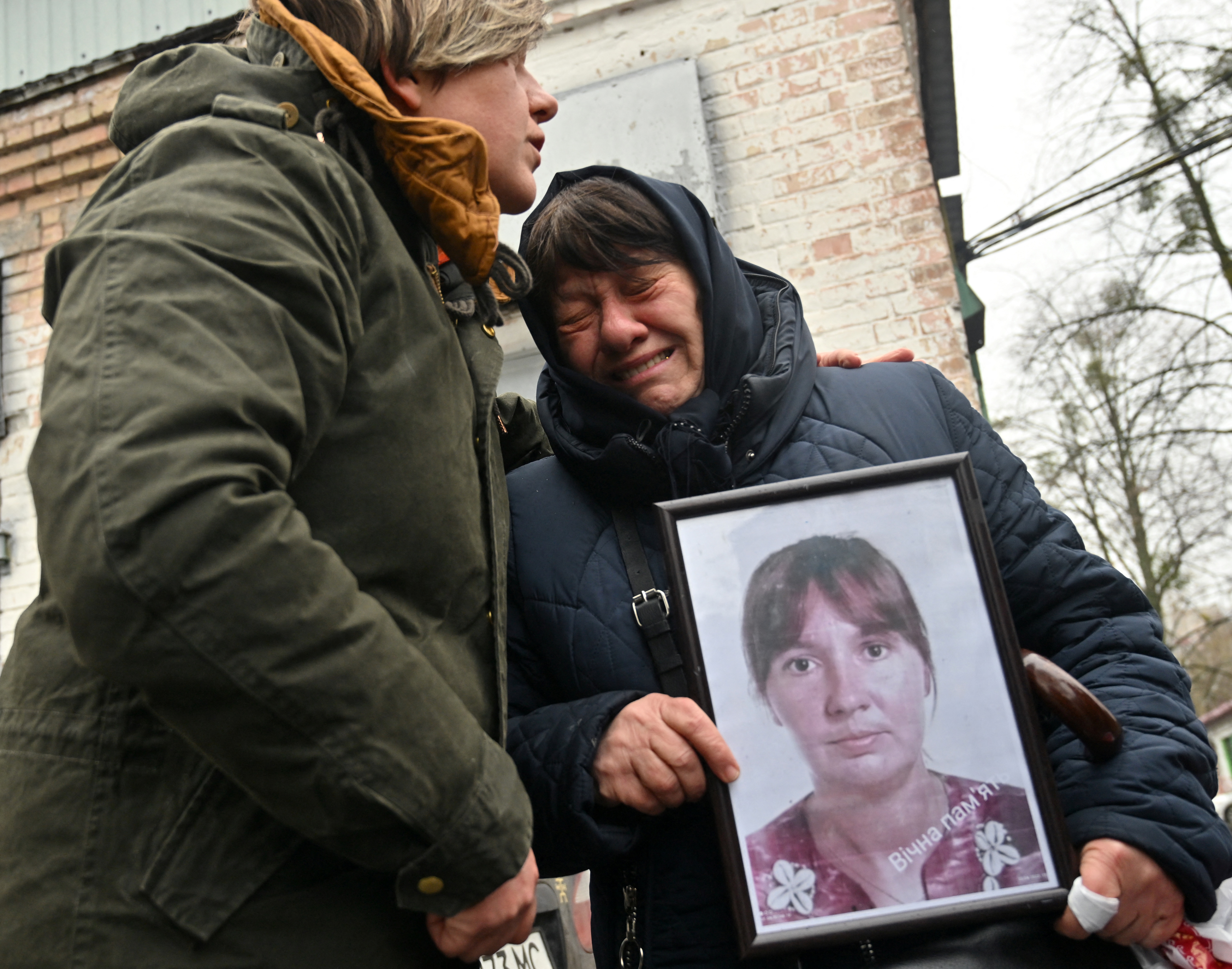 A woman cries as she holds a photograph of her adult daughter who was killed in Bucha in Ukraine