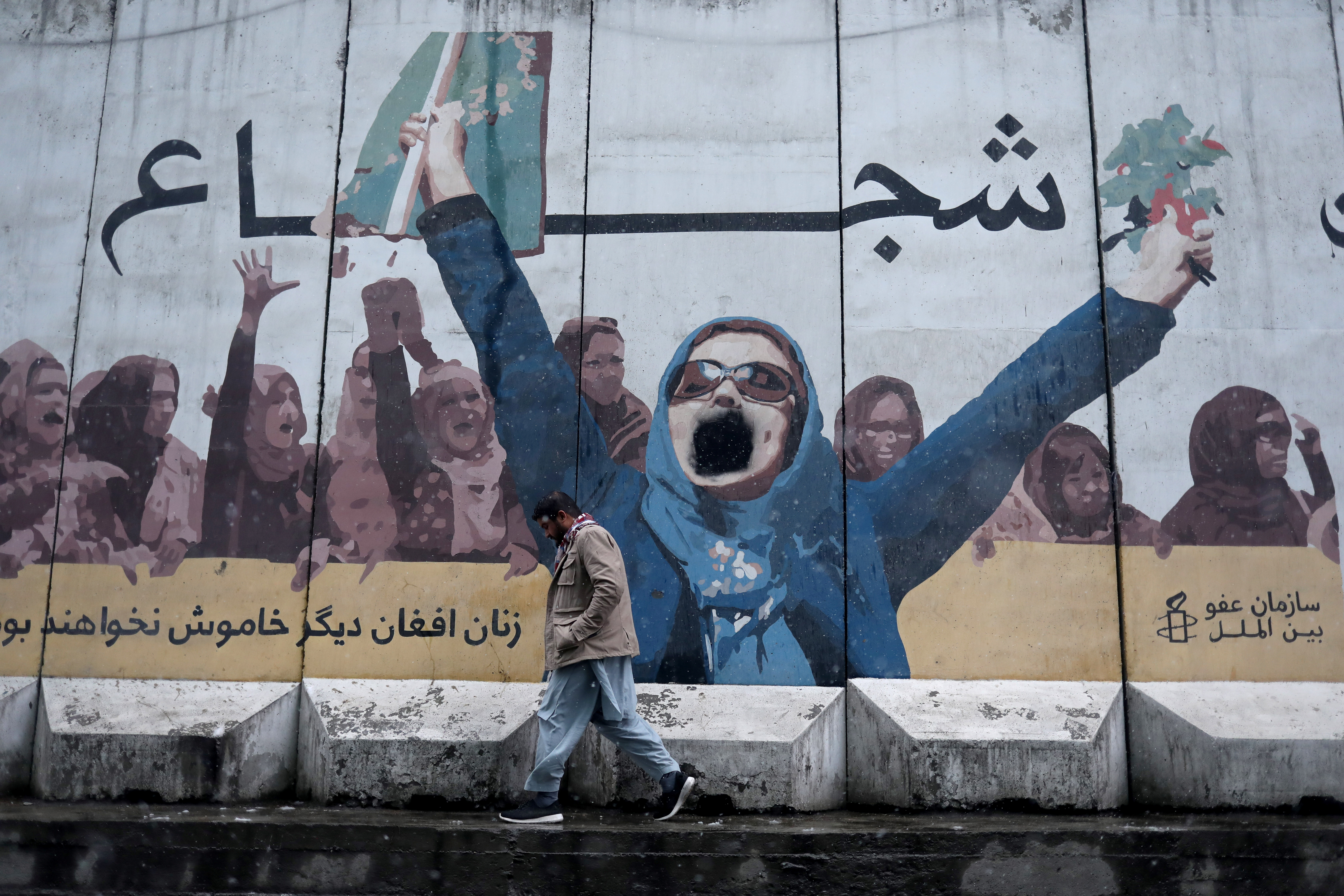 A man walks past a painting on the wall of the former embassy for women's affairs in Kabul, Afghanistan, January 3, 2022. The painting reads on the top "Brave" and bottom - "Afghan women no longer silent".