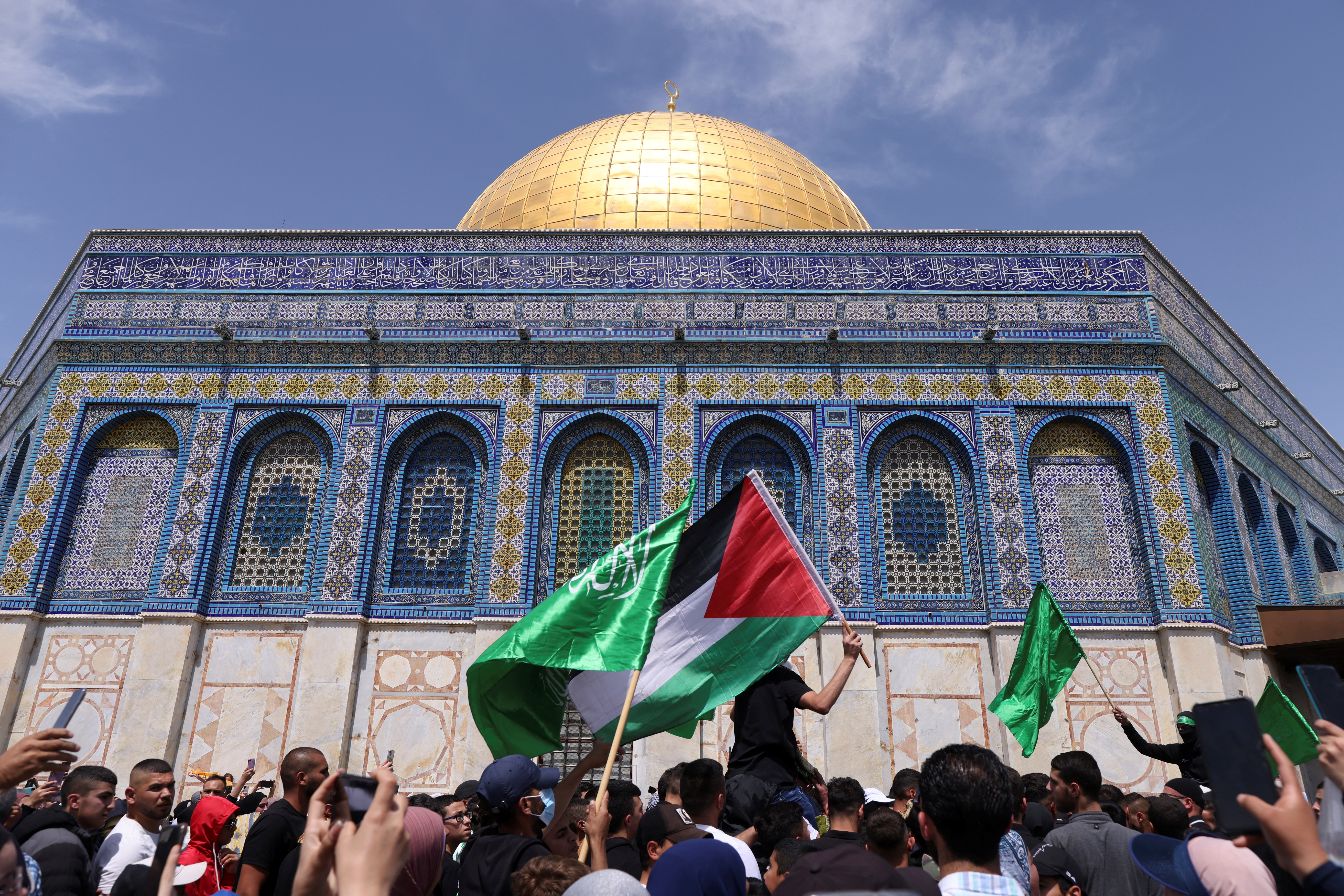 Palestinians raise flags in protest at the compound that houses Al-Aqsa Mosque
