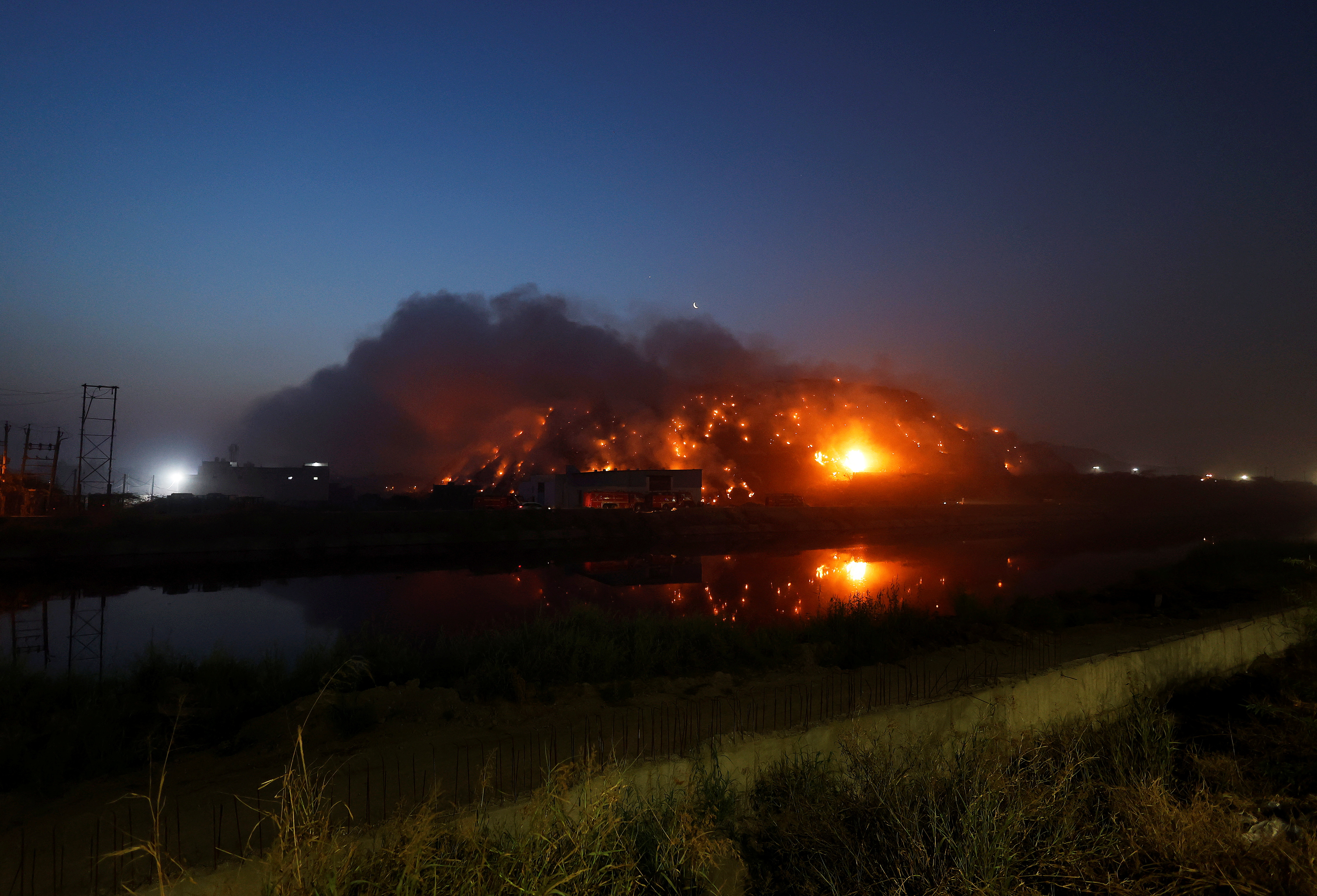 Fire trucks seen on a road as smoke billows from burning rubbish at the landfill site