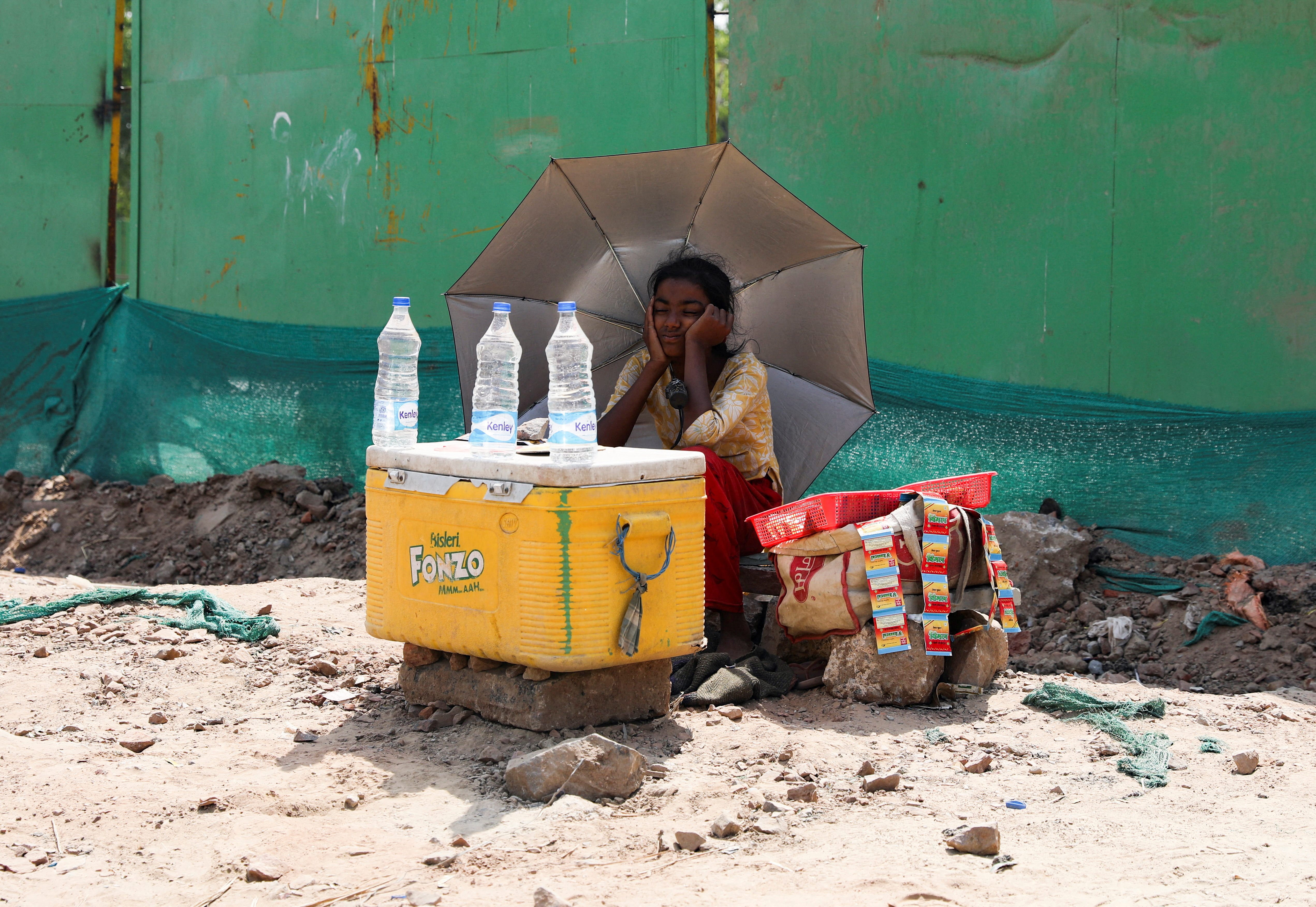A girl selling water uses an umbrella to protect herself from the sun as she waits for customers on a hot summer day in New Delhi