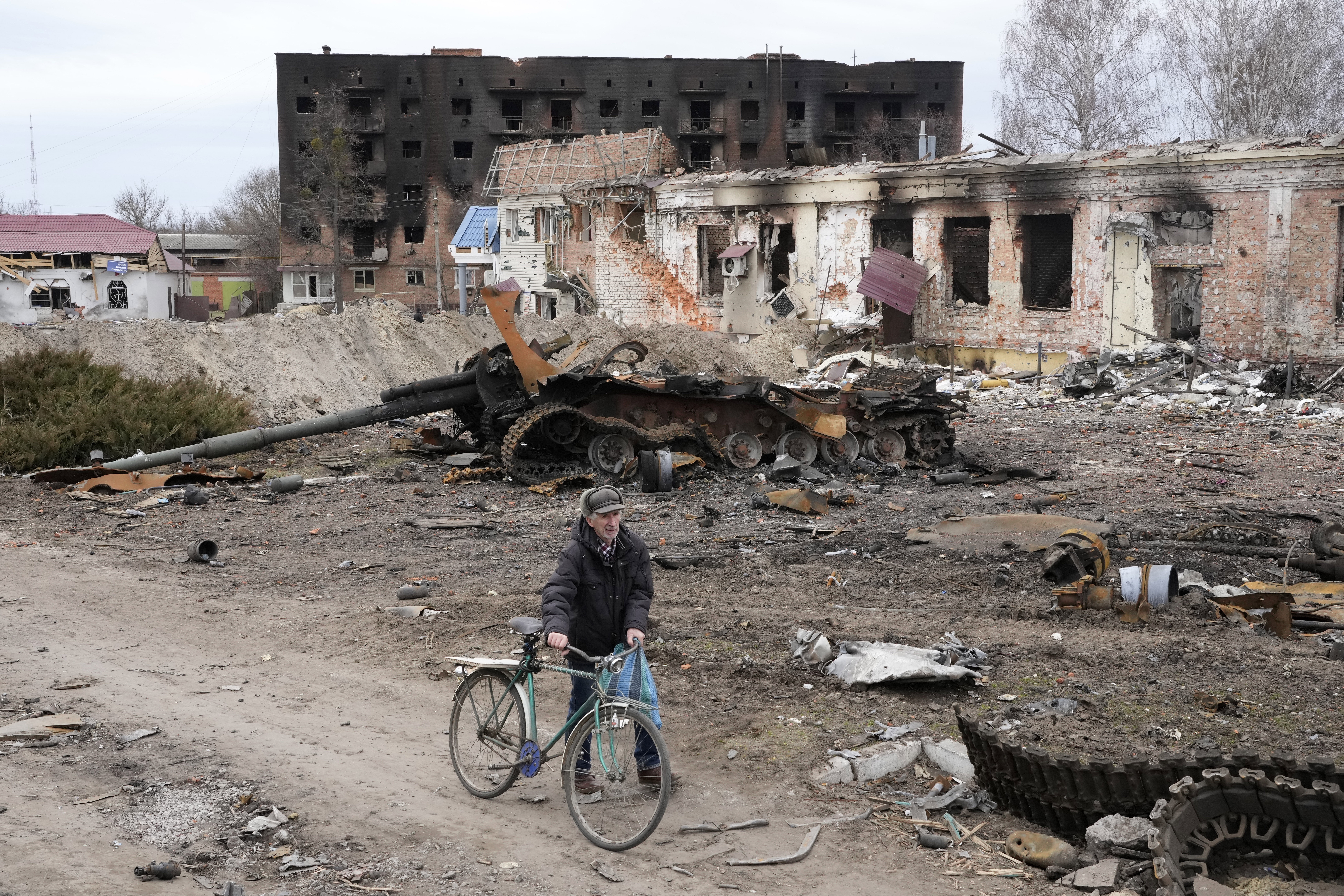 A local resident passes with his bicycle in front of damaged buildings and a tank in the town of Trostsyanet