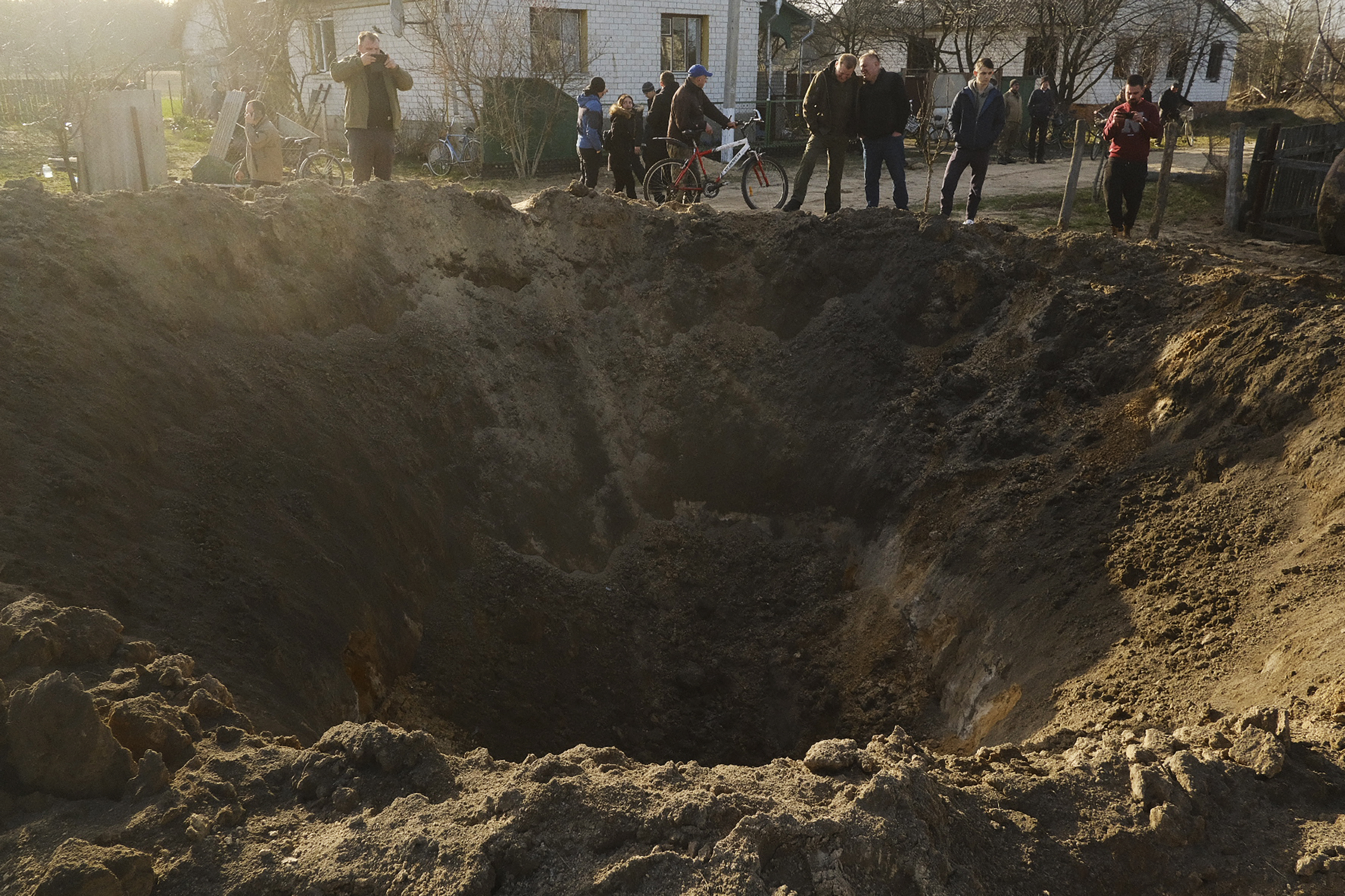 People look at a crater of an explosion in the village of Horodnya, Chernihiv region on Thursday