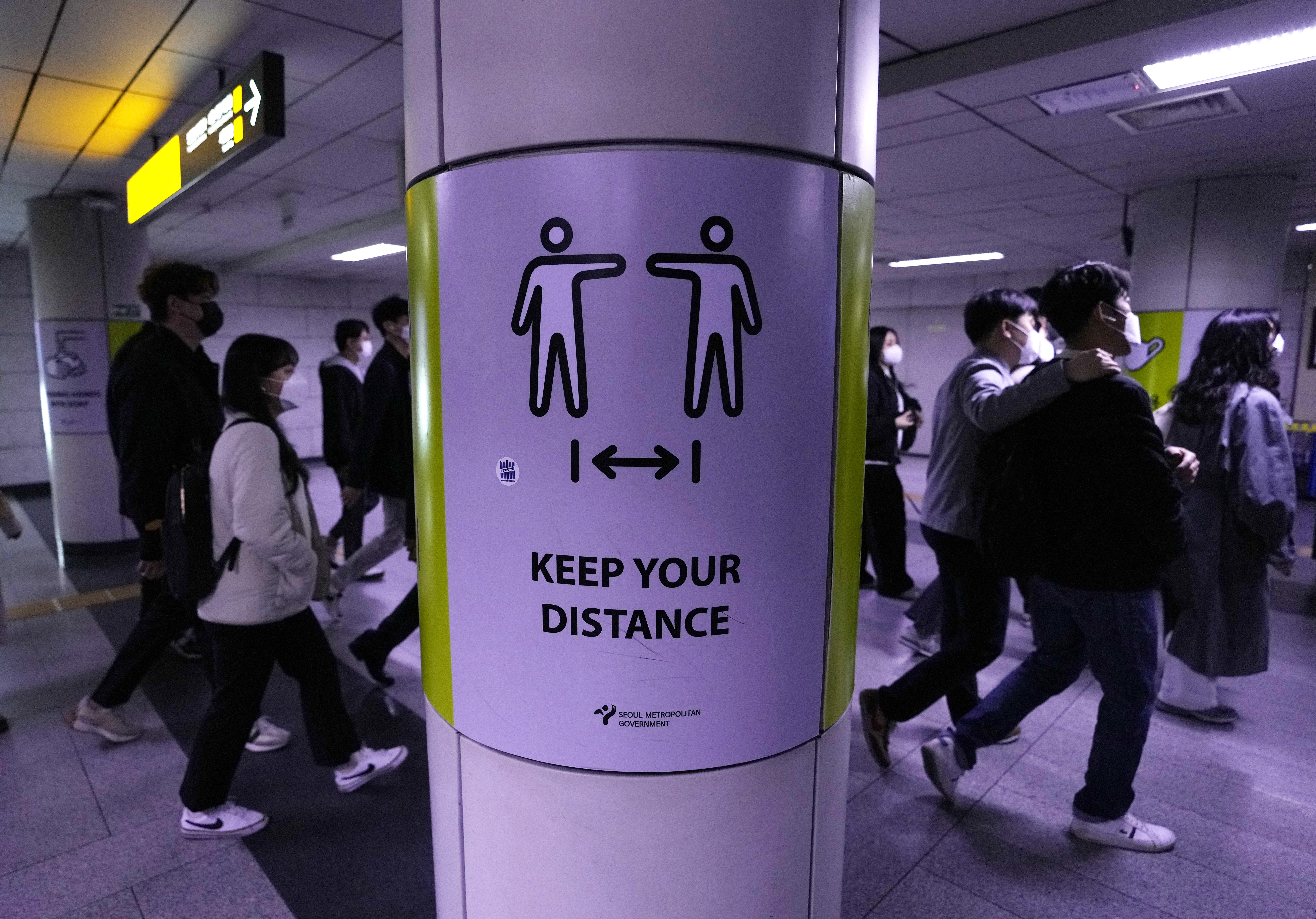 People wearing face masks pass by a poster urging precautions against the coronavirus at a metro station in Seoul. Most restrictions will be lifted on Monday