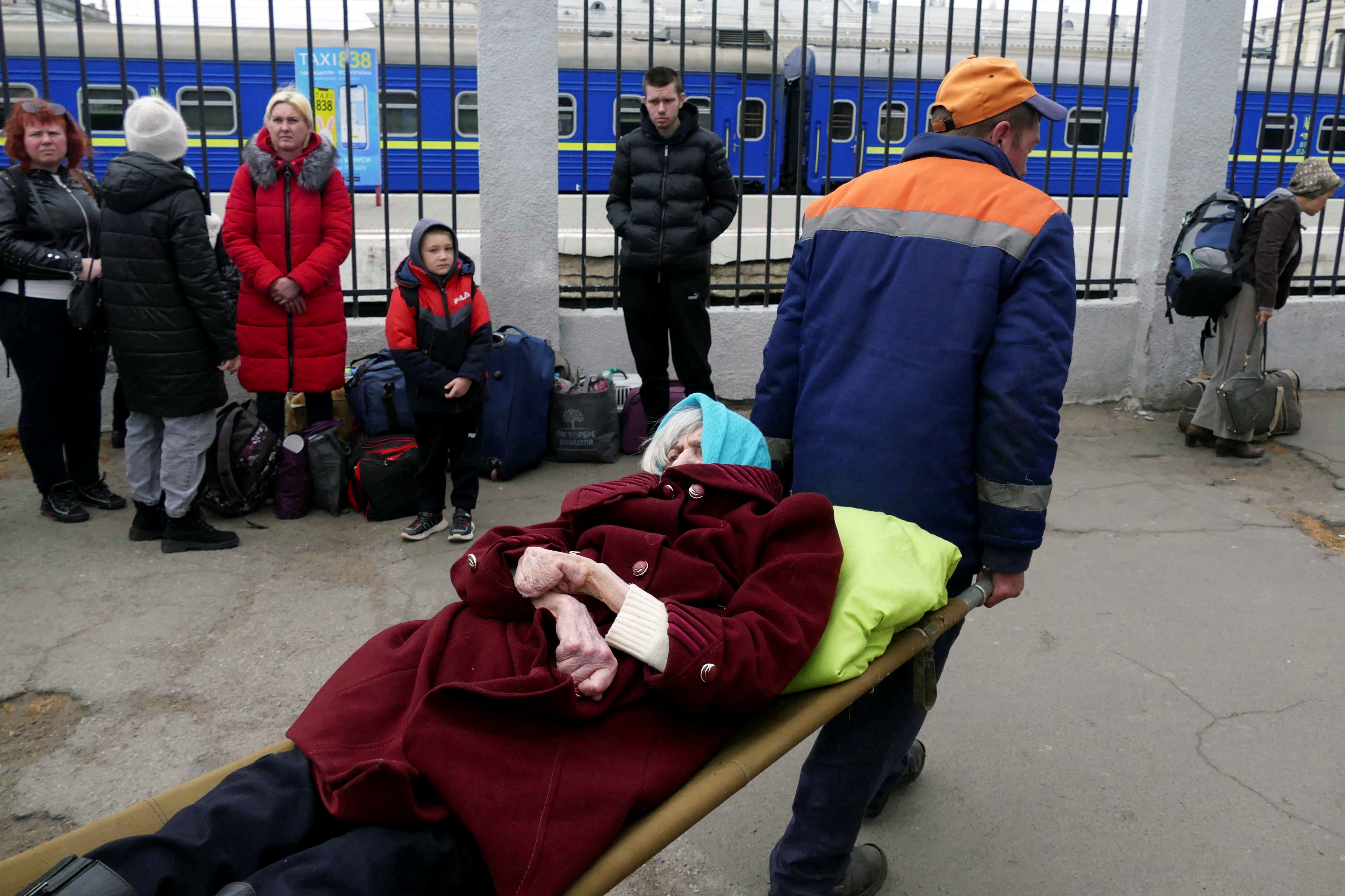 Men carry an elderly woman as residents from Mykolaiv arrive by bus in Odesa, after being evacuated following shelling on April 16, 2022