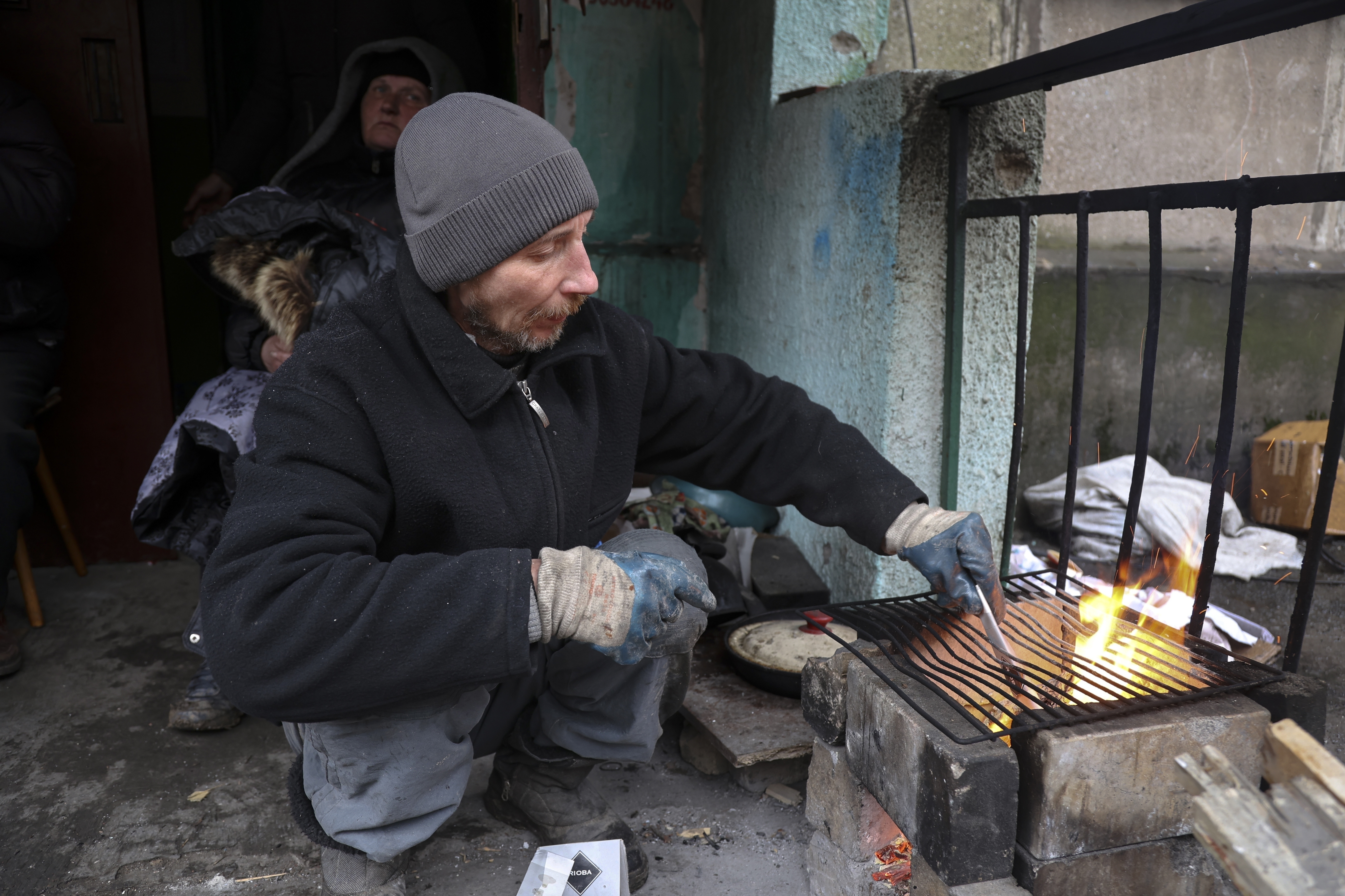 Resident in Mariupol prepares to cook at an entrance of a building damaged during fighting, April 13, 2022