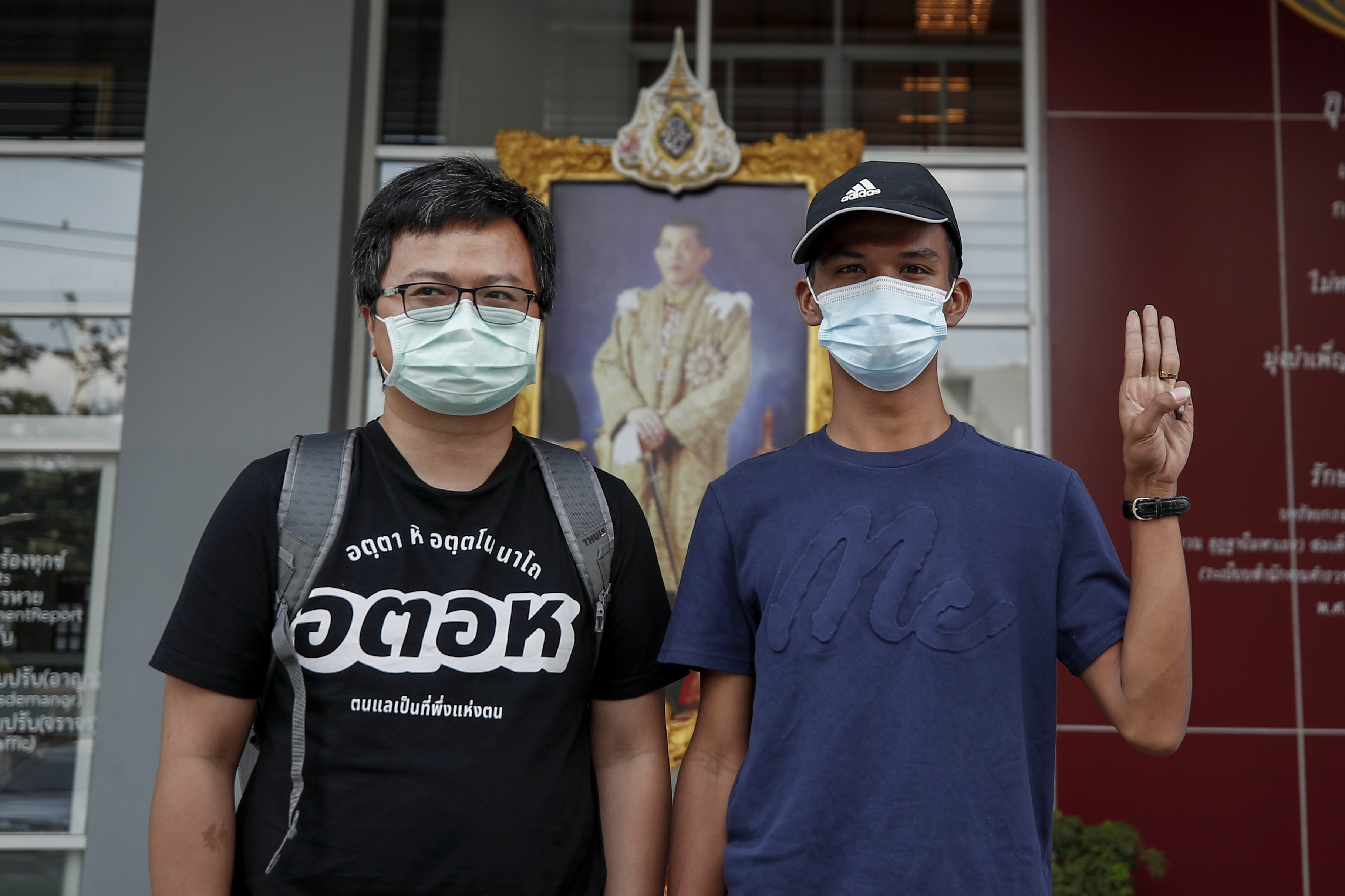 Pro-democracy protest leaders Anon Nampa (L) and Panupong 'Mike' Jadnok who is making the three-finger salute stand in front of an official portrait of Thailand's king