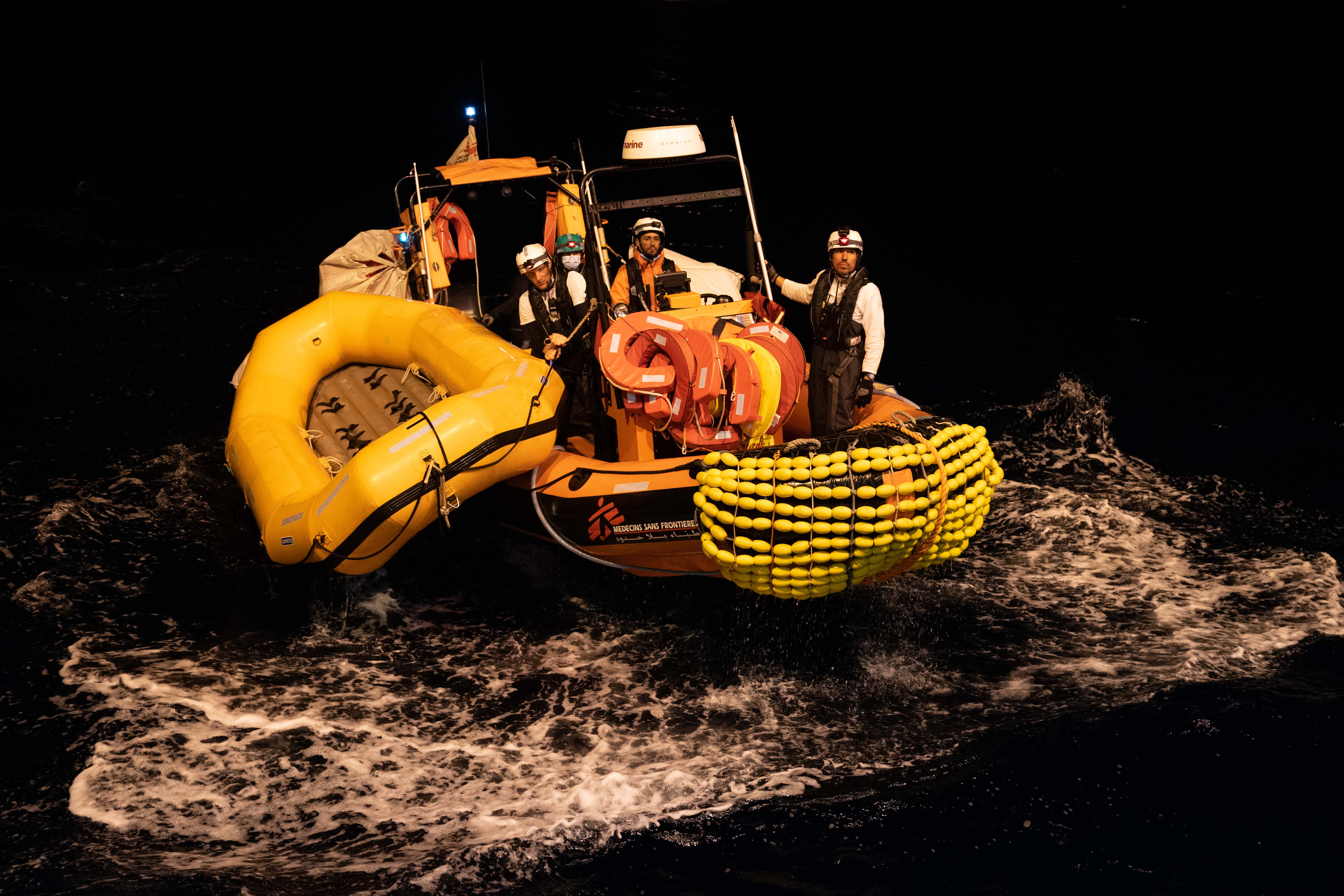 A photo of a boat with a search and rescue team with an empty lifeboat tied to the boat in dark waters.