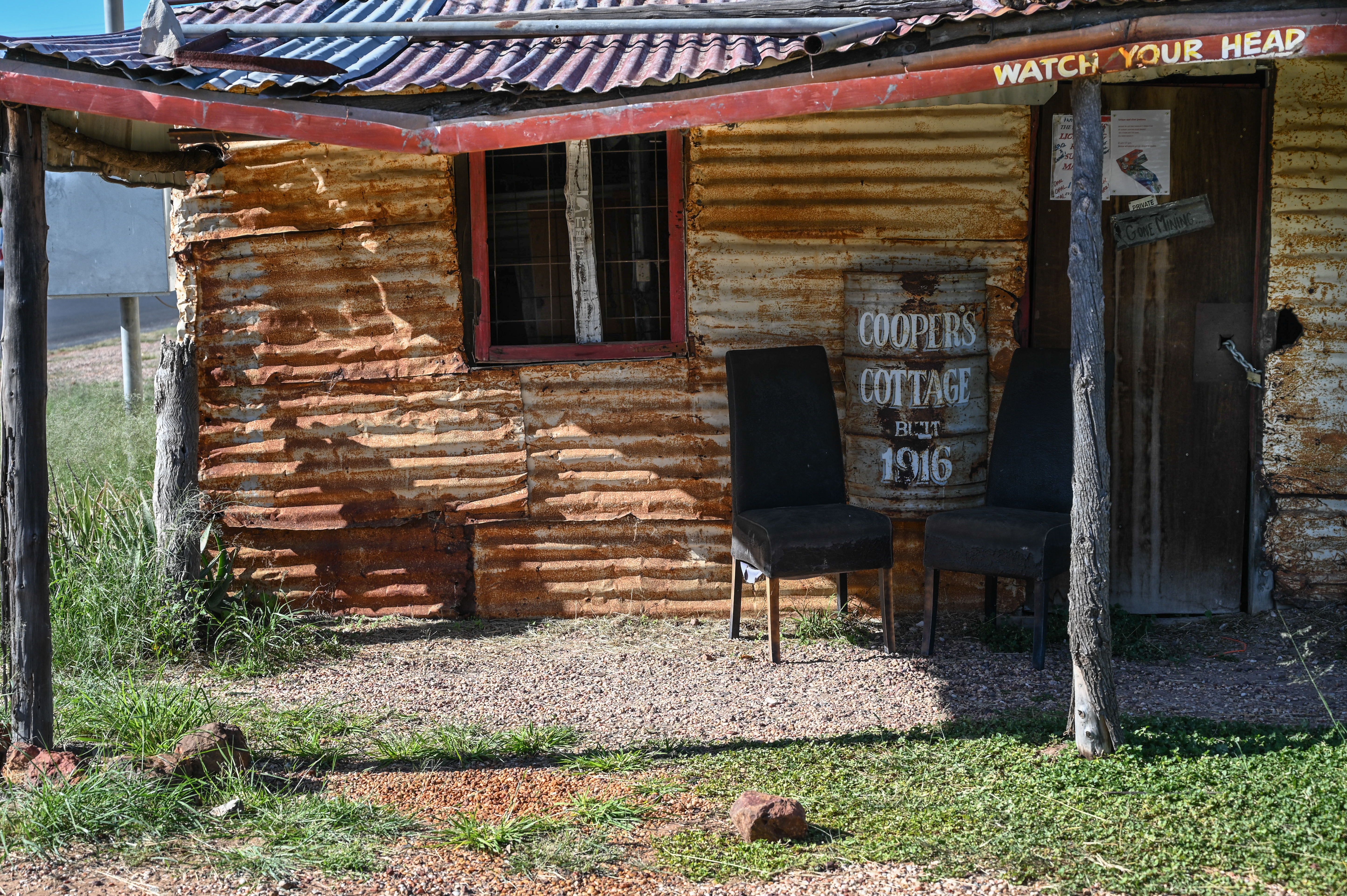 A photo of Coopers Cottage with a sign next to a chair that says "Coopers Cottage 1916".