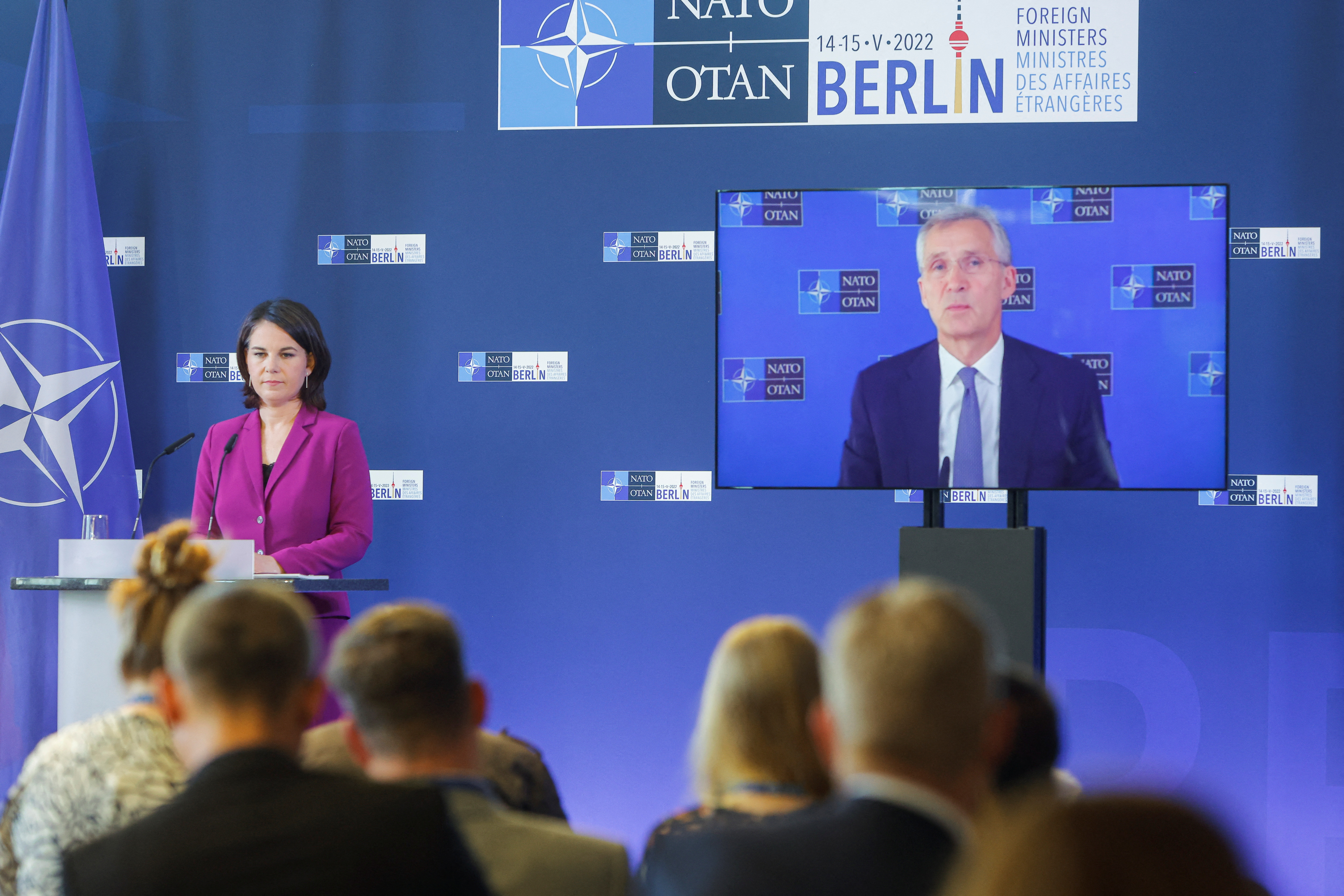 NATO Secretary-General Stoltenberg is seen on a screen speaking during a news conference at a NATO meeting, while German foreign minister Annalena Baerbock stands at a podium, in Berlin, Germany