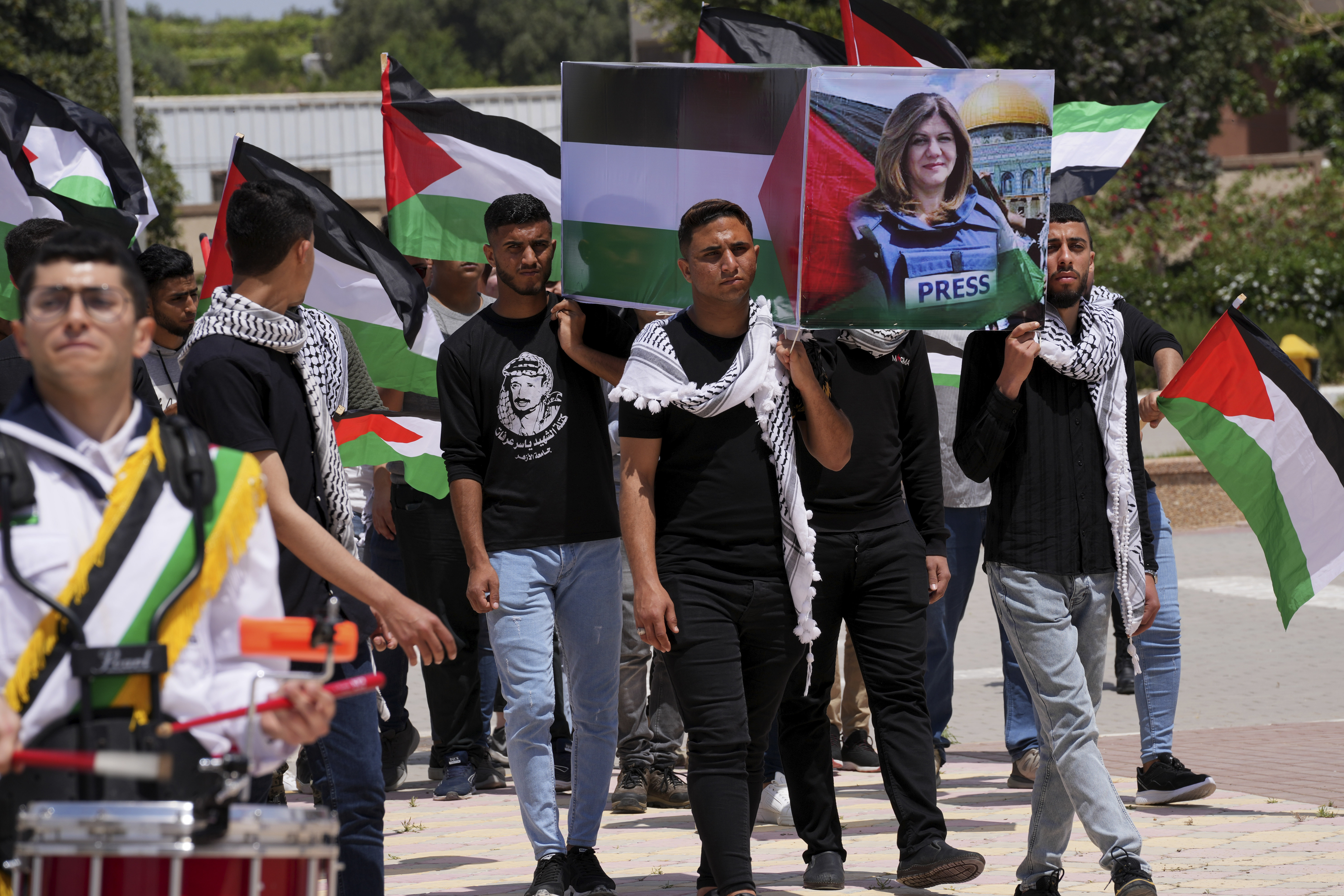 A youth beats a drum while students carry a mock coffin during a symbolic funeral for slain Al Jazeera journalist Shireen Abu Akleh, as others wave their national flags at al-Azhar University in Mughraqa, central Gaza Strip, May 16, 2022.