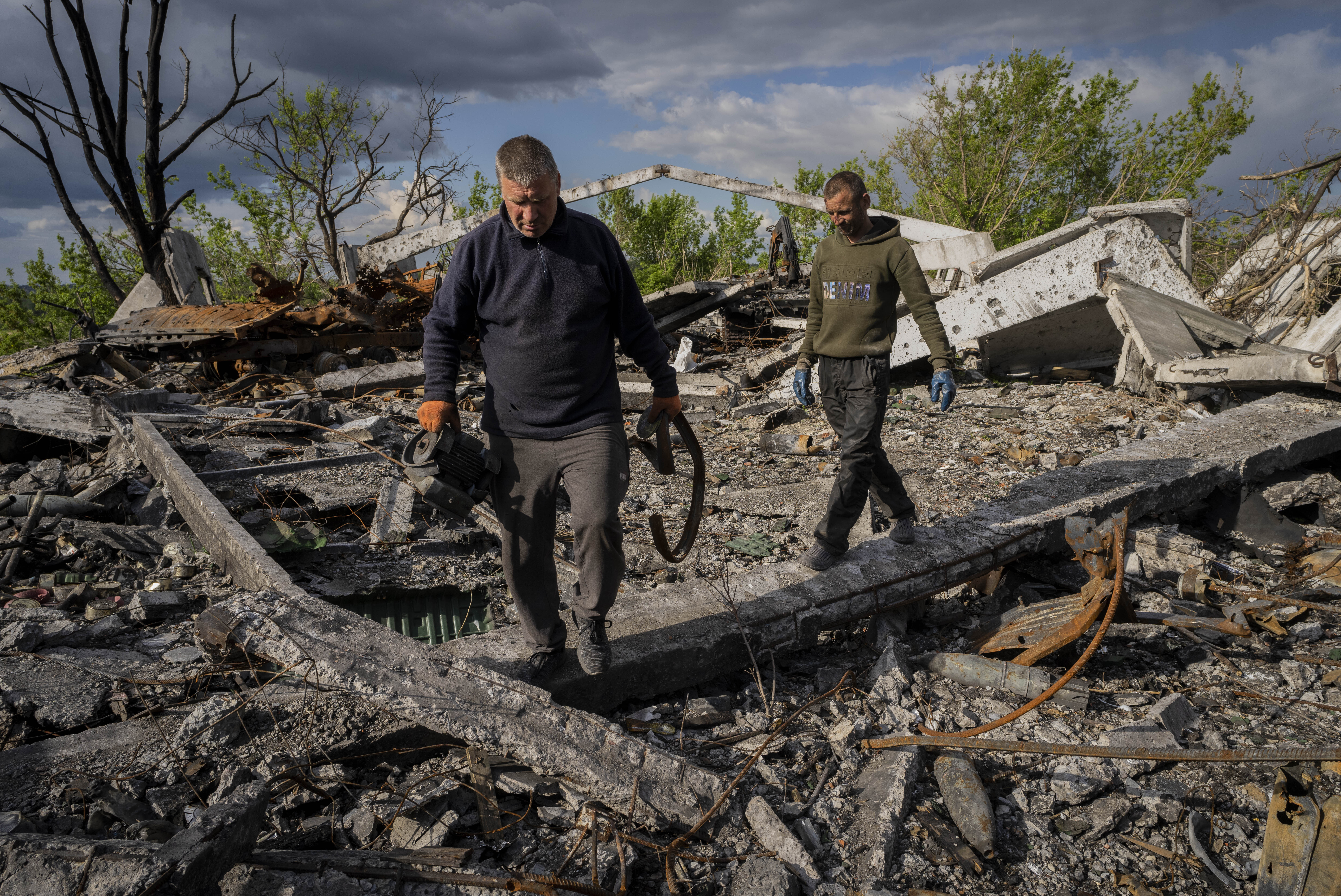 Villagers walk past unexploded artillery shells as they collect scrap metal from a bombed warehouse in the village of Malaya Rohan, Kharkiv region, May 18, 2022