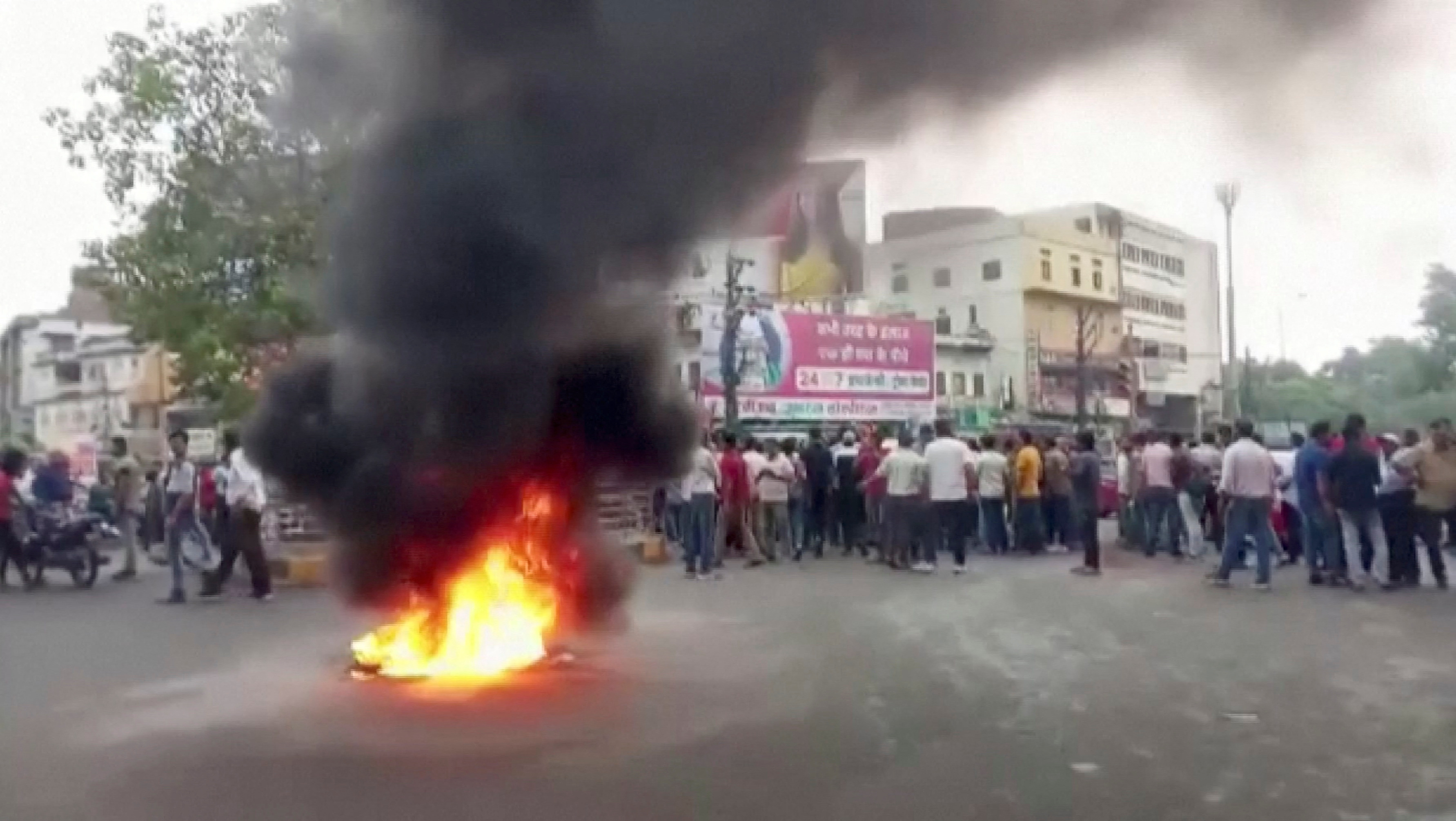 Smoke rises from a burning material as people gather on a road amid tensions over Lal’s killing in Udaipur
