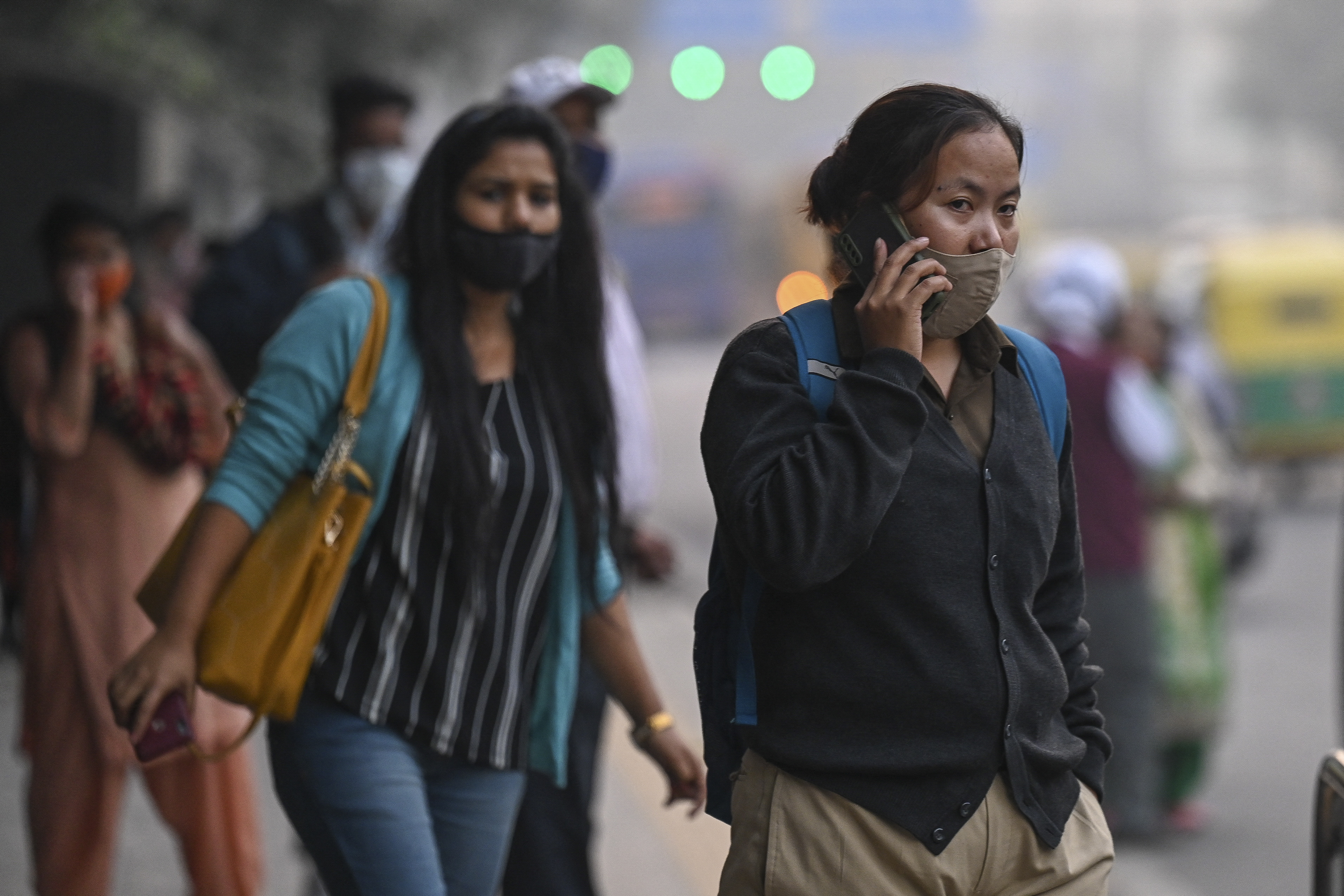 Two women, one on a mobile phone, wait for a bus in New Delhi