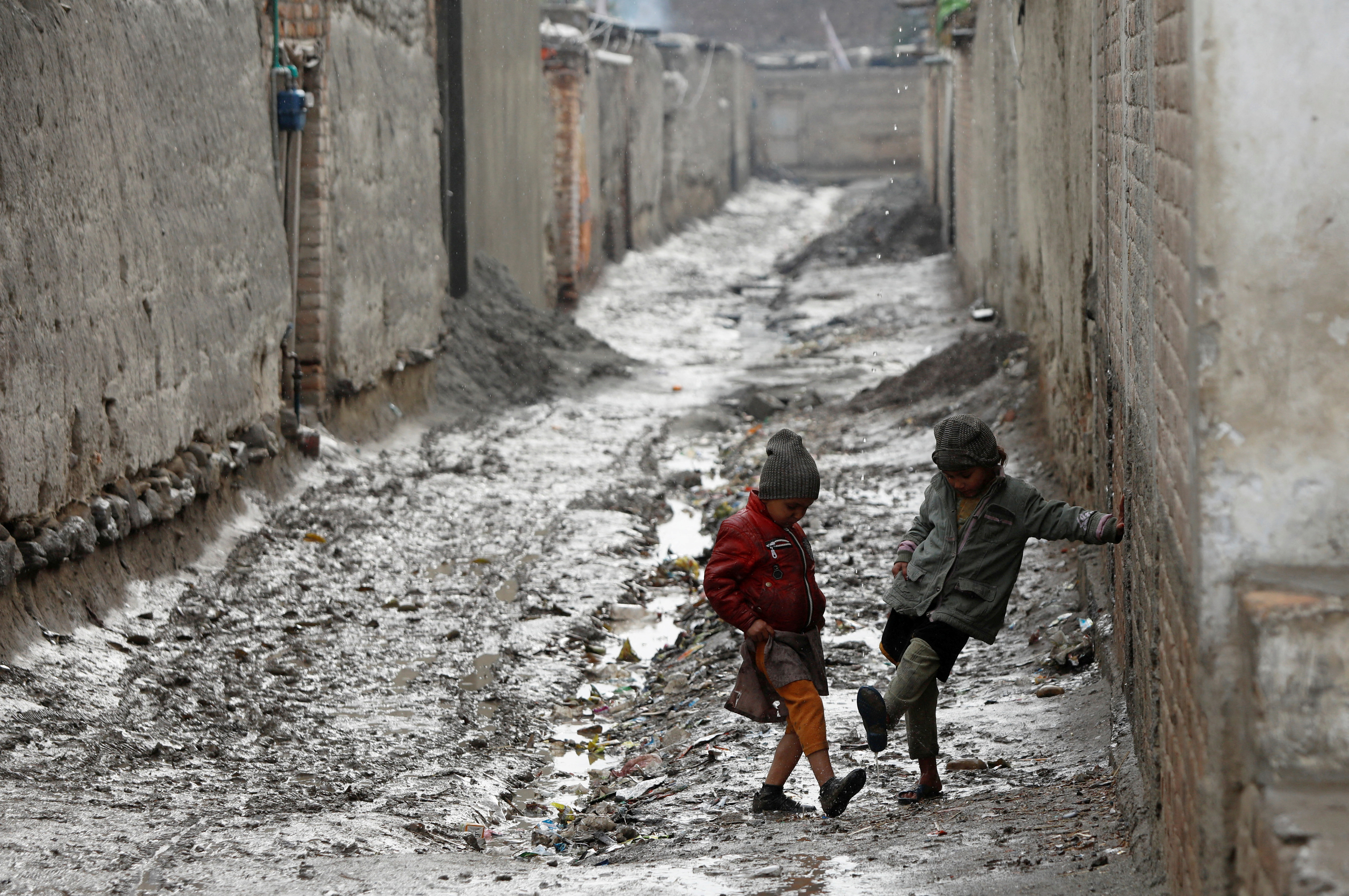 Children play along a muddy street after rain in Peshawar