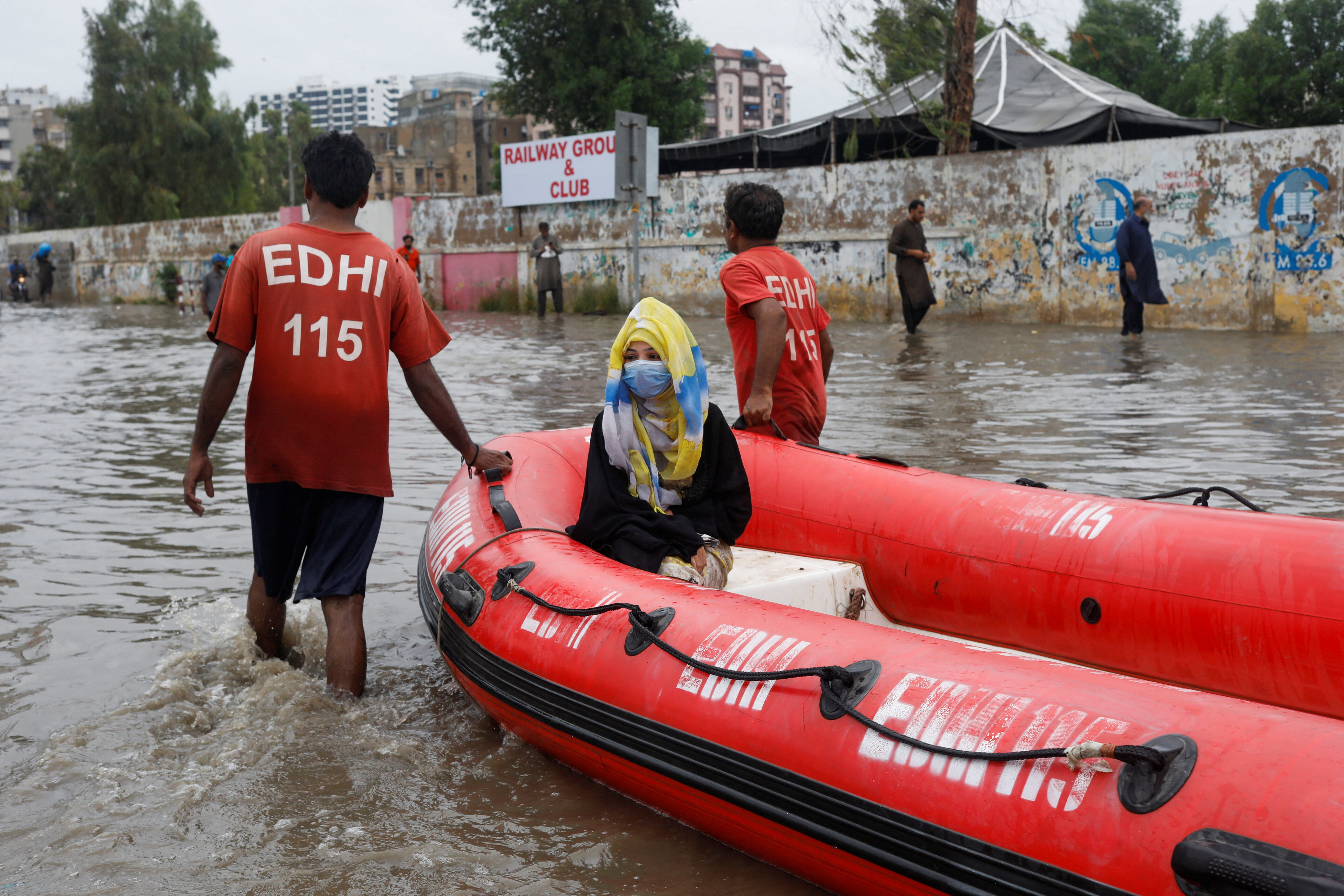 A woman sits in a rubber boat pulled by volunteers on a flooded road in Karachi