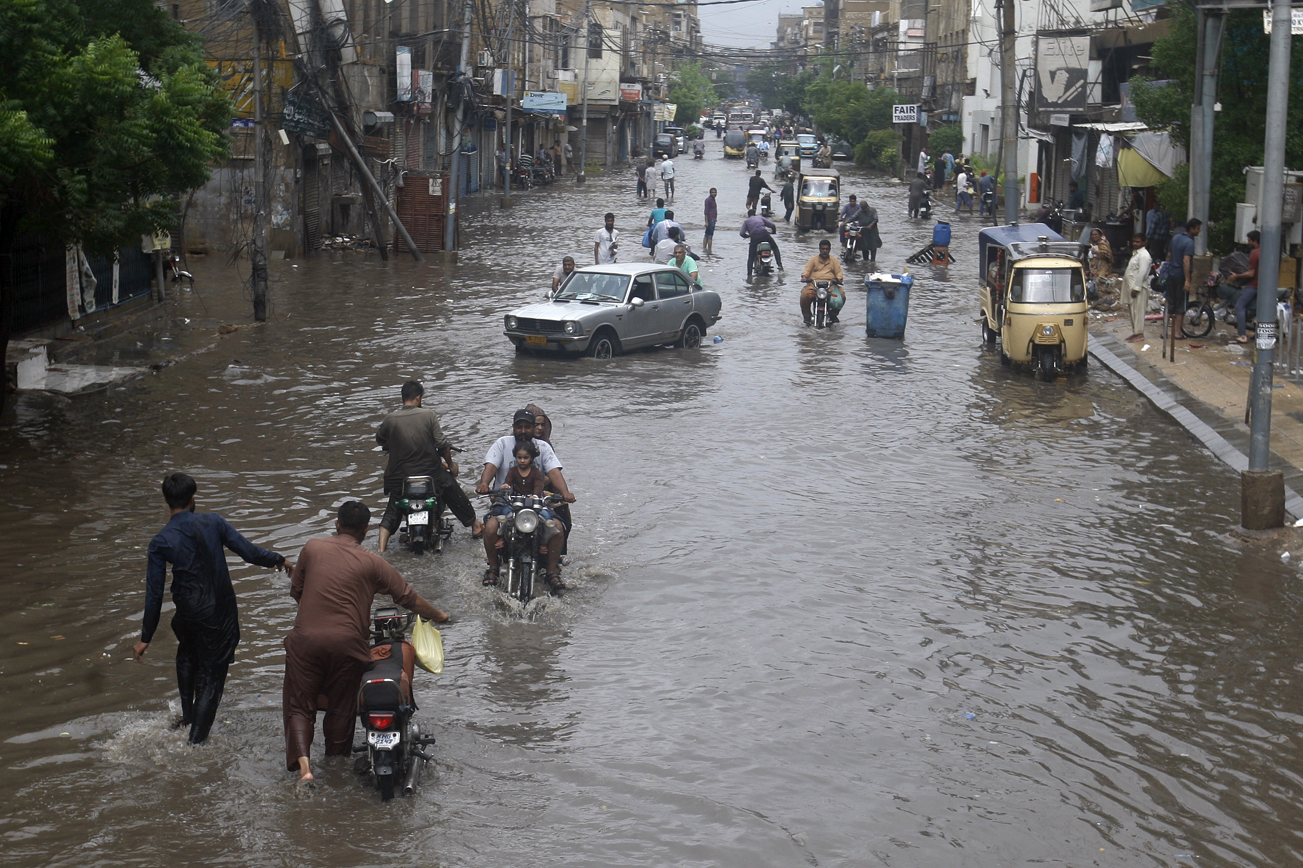 Vehicles and people wade through a flooded road in Karachi