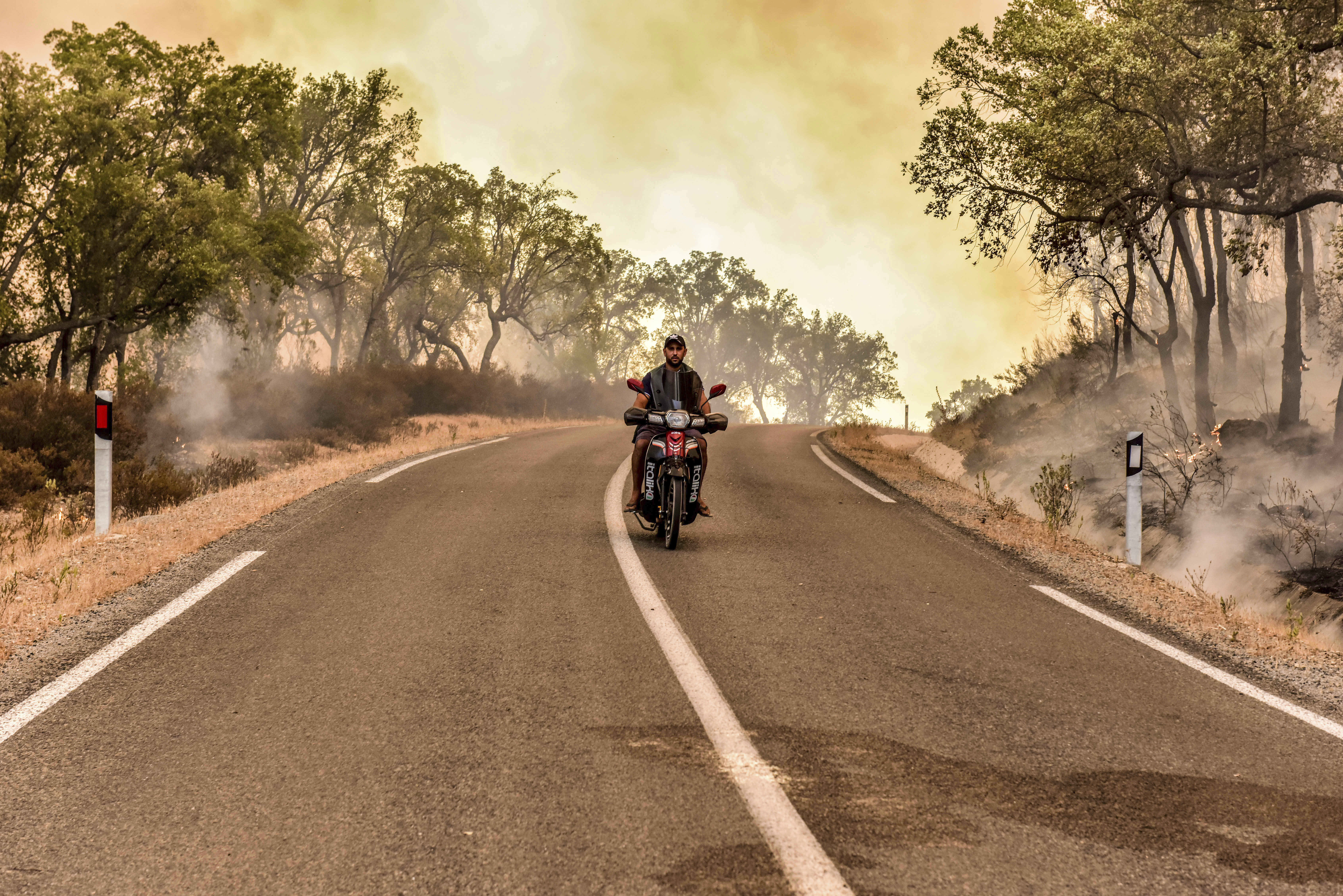 A man drives through a highway as a wildfire rages that was caused by extreme temperatures, in Larache, northern Morocco,