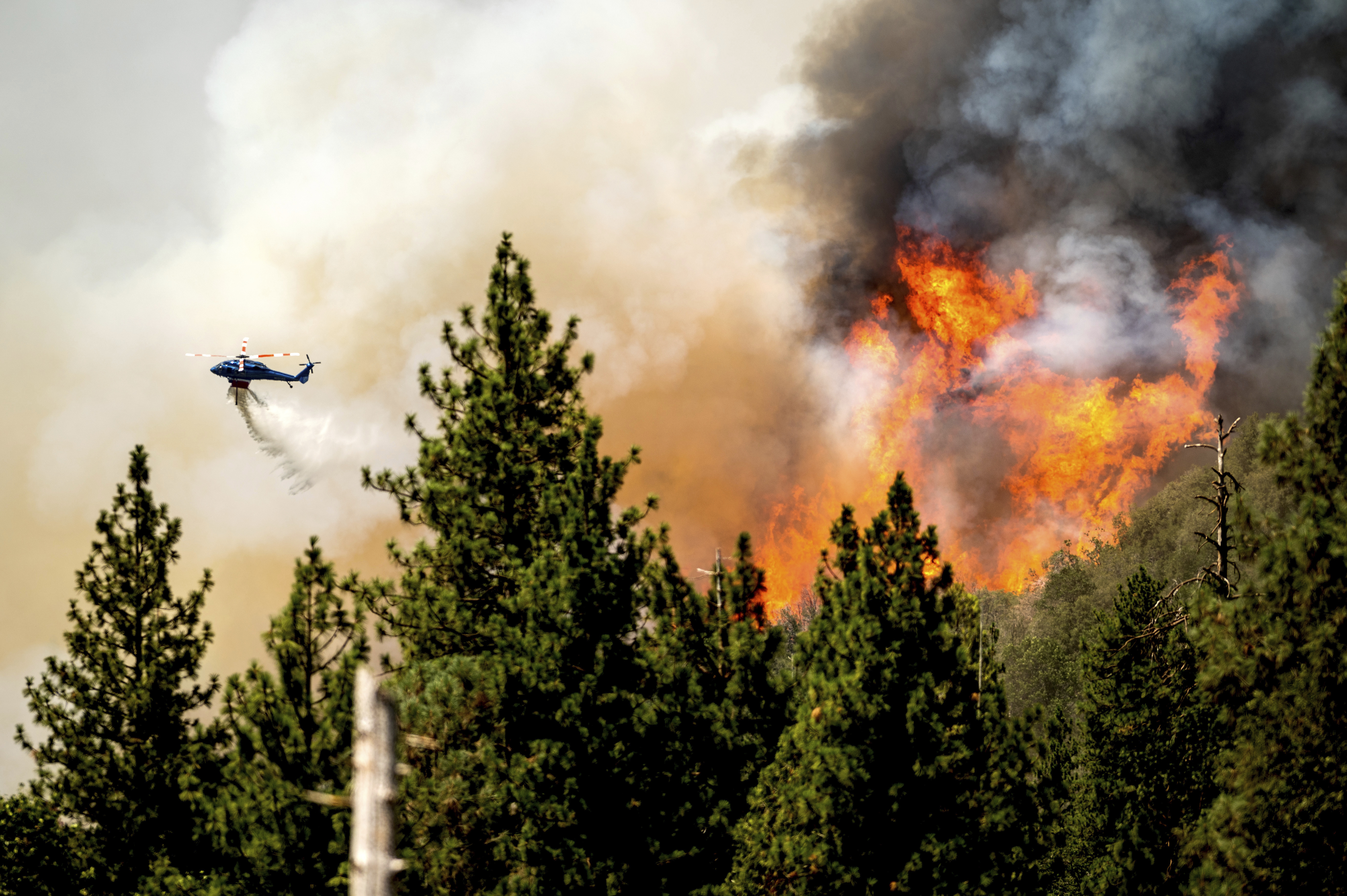 A helicopter drops water while battling the Oak Fire in Mariposa County on Sunday