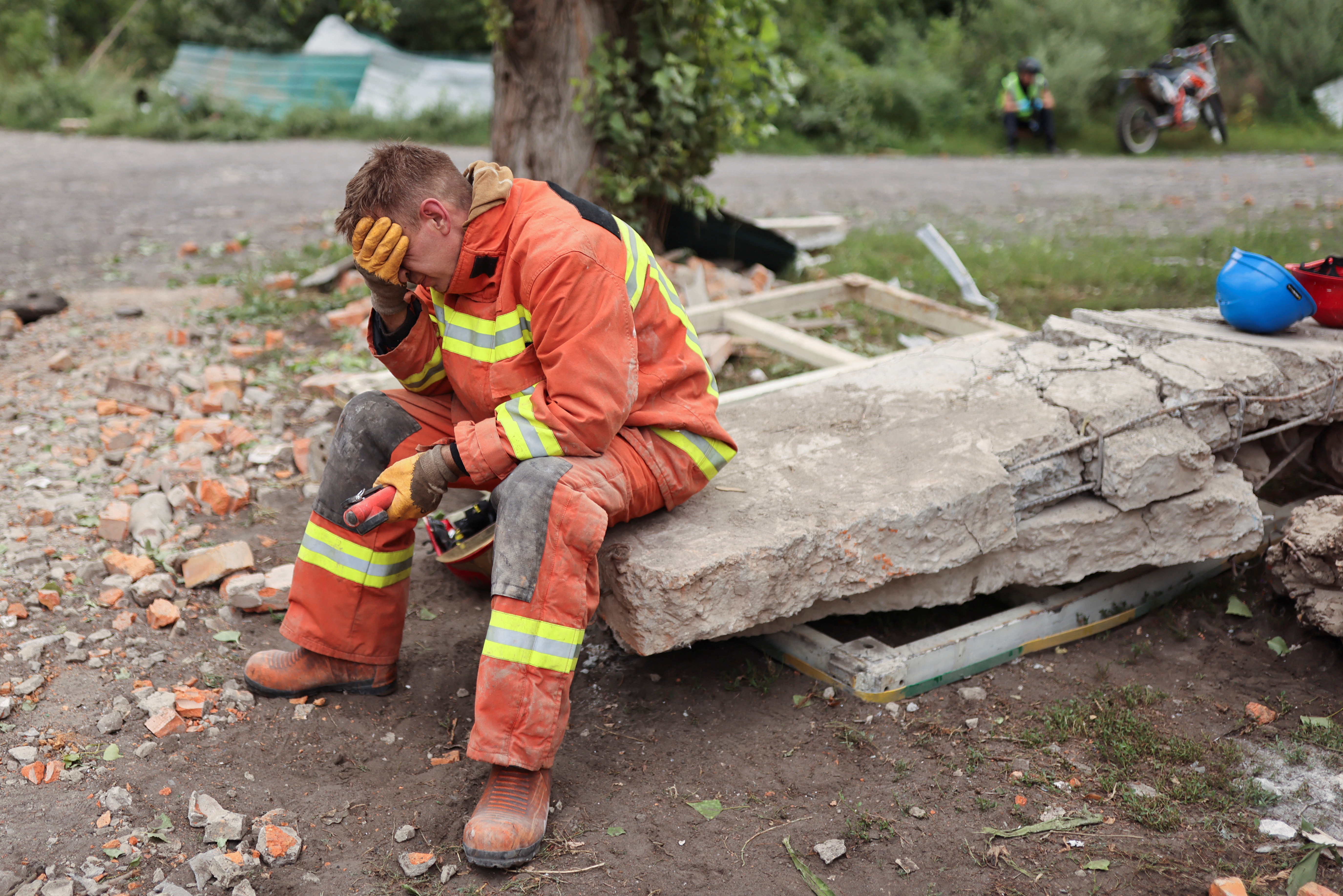 A man sits as firefighters remove debris to find bodies of people at the Central House of Culture, after a military raid hit a building in Chuhuiv, Ukraine.