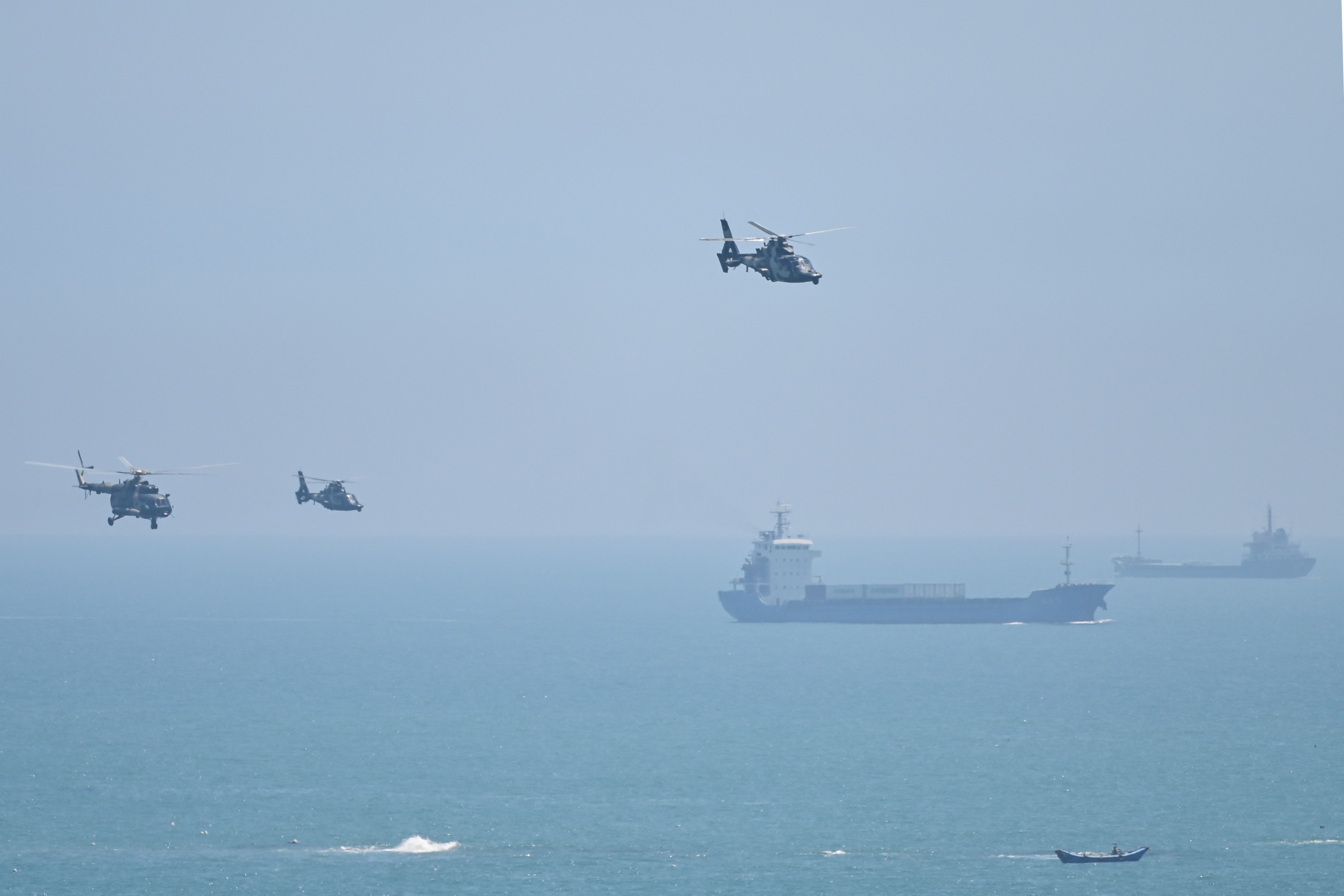 Three Chinese helicopters in the air with what look like commercial shipping vessels below off China's Pingtan island