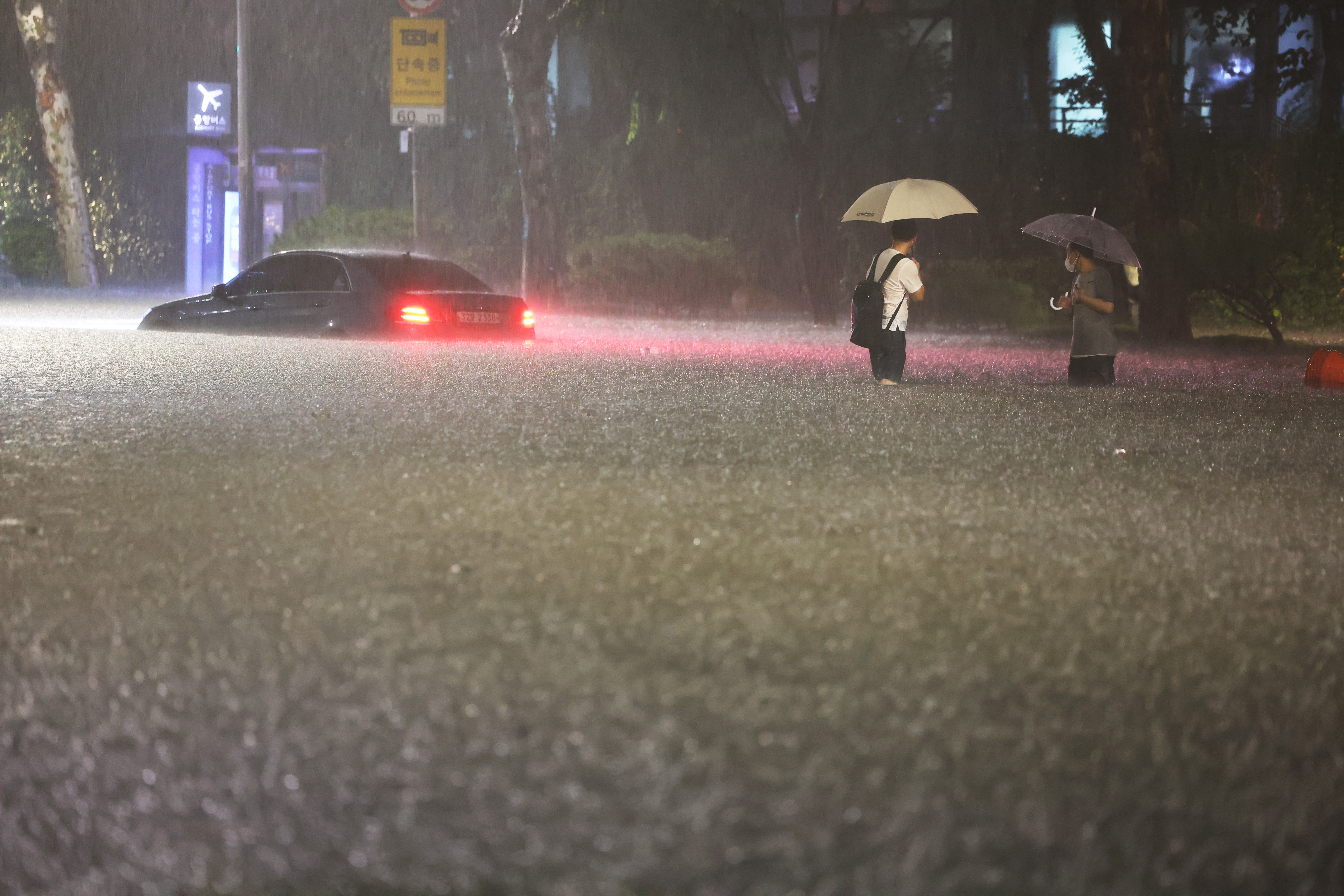 People wade alongside submerged cars in a street during heavy rainfall in the Gangnam district of Seoul on August 8, 2022.