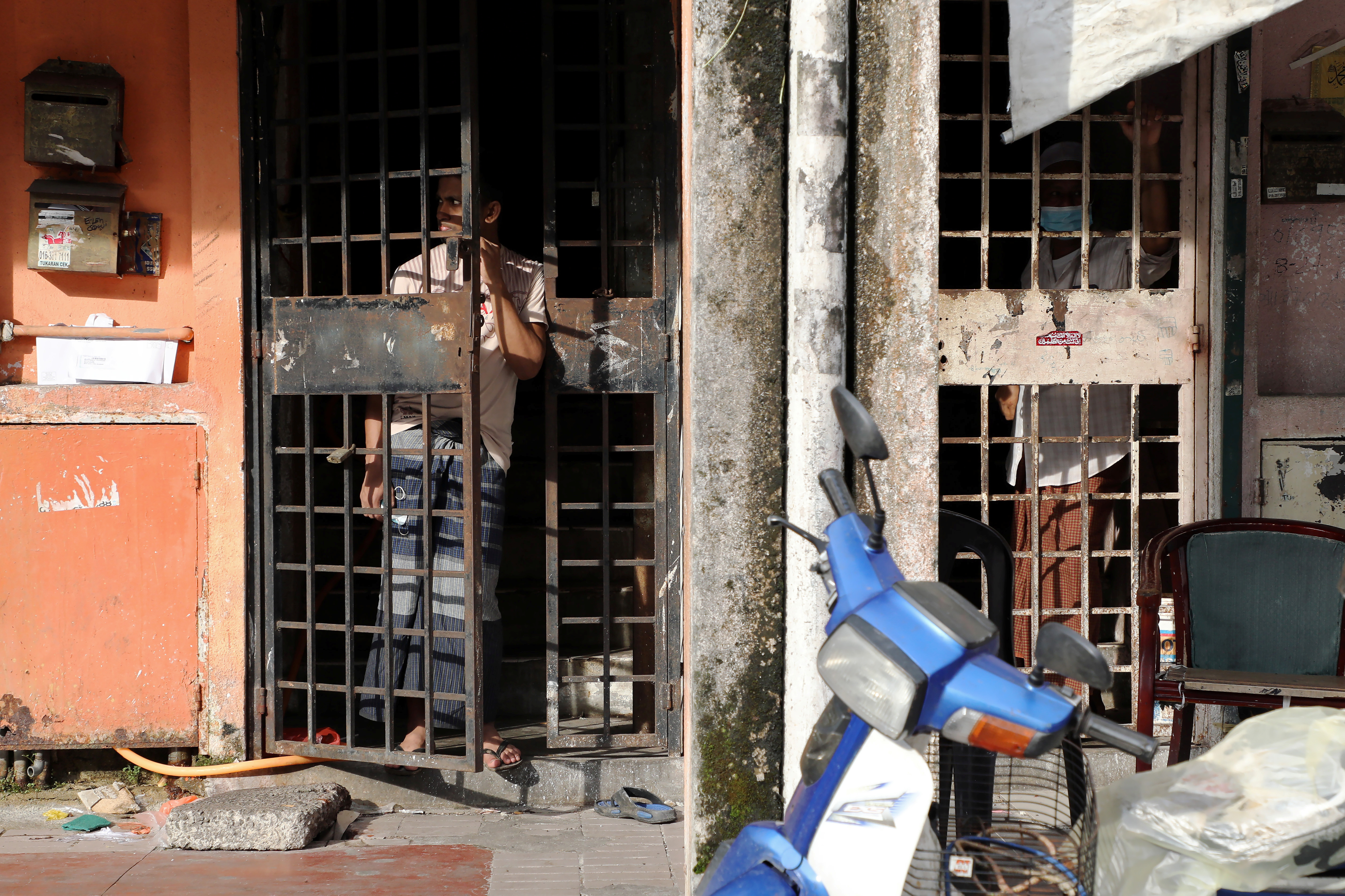 A refugee in Kuala Lumpur watches the street from behind a security gate on his door