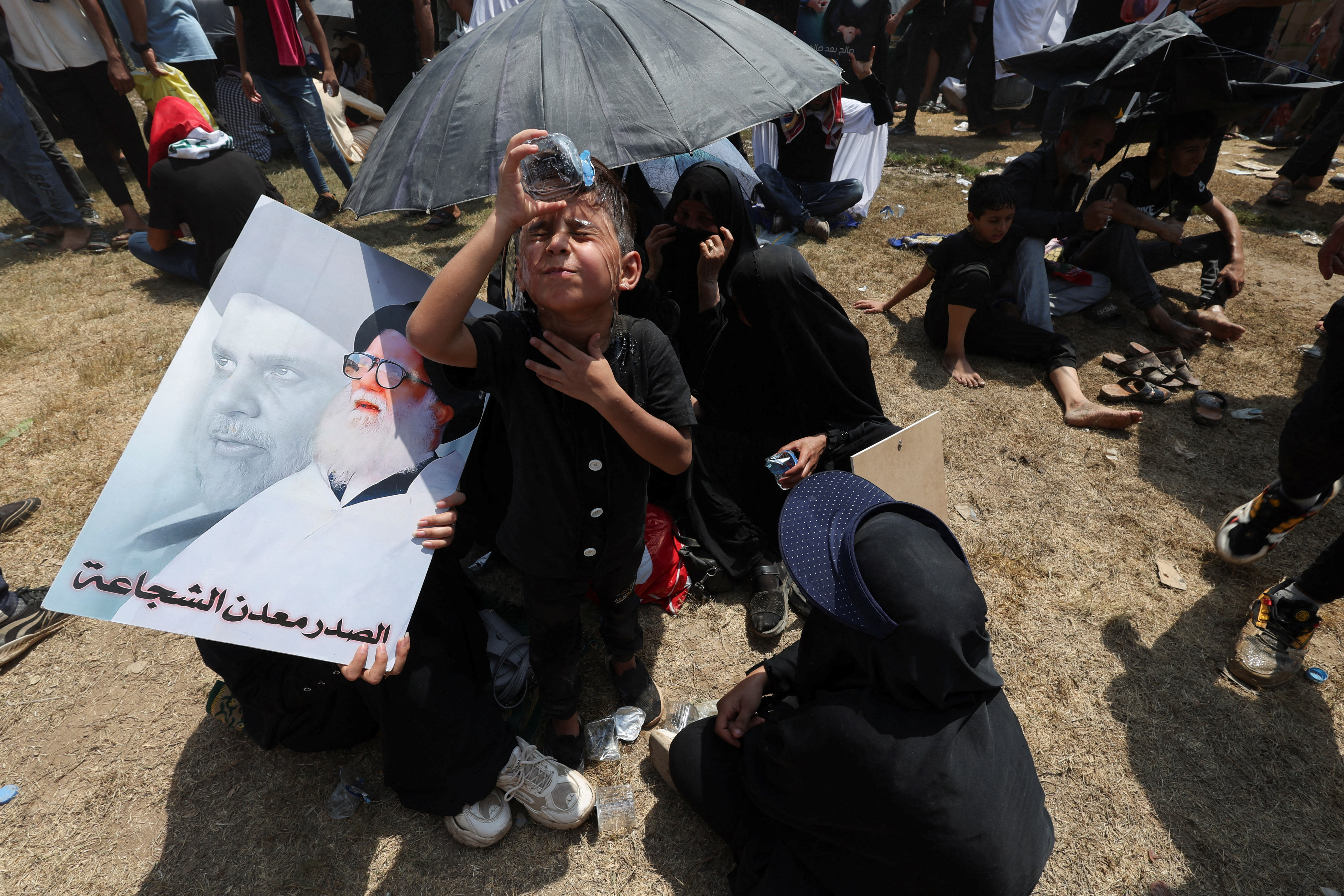 A boy pours water in his Muqtada al-Sadr gather for mass Friday prayer on August 5, 2022 [Alaa al-Marjani/Reuters]